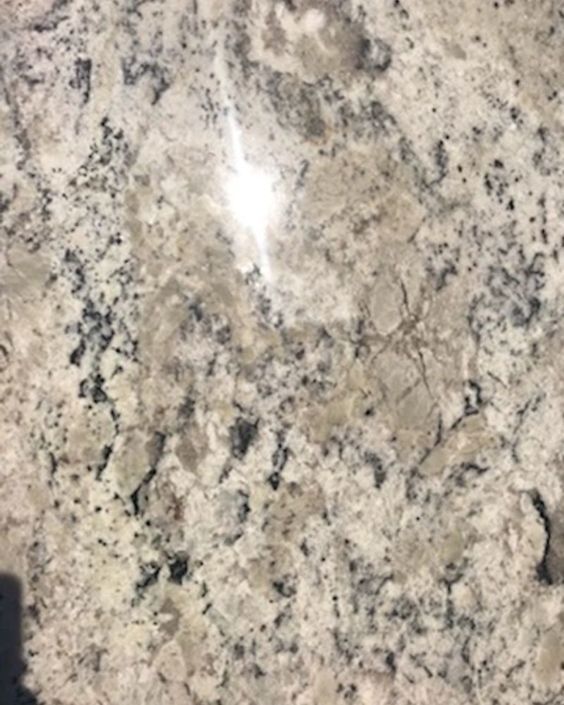 Close-up of polished beige granite with gray and black speckles and a bright light reflection