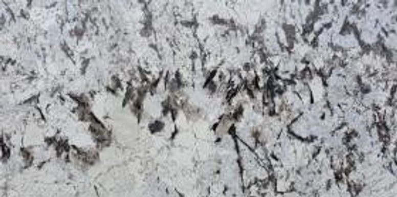 Snow-dusted gray stone surface with scattered dark cracks and specks
