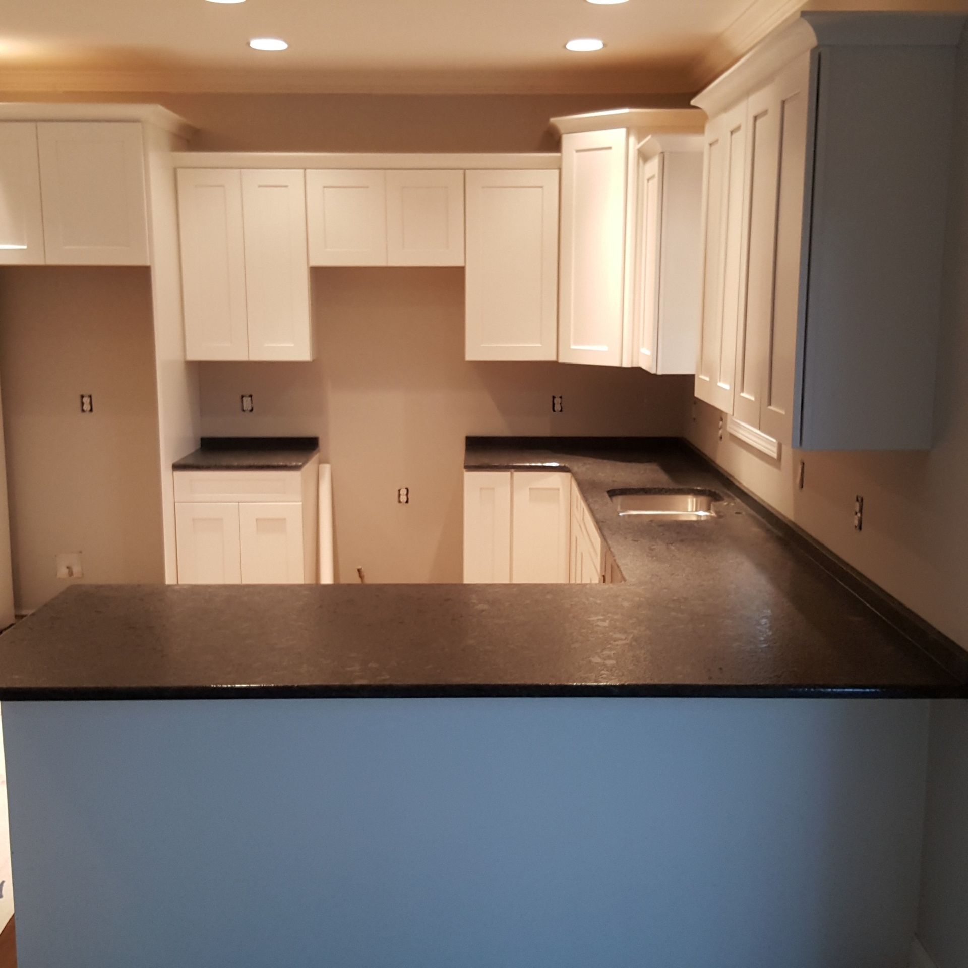 Empty kitchen with white cabinets, dark countertops, and a black island under warm recessed lighting