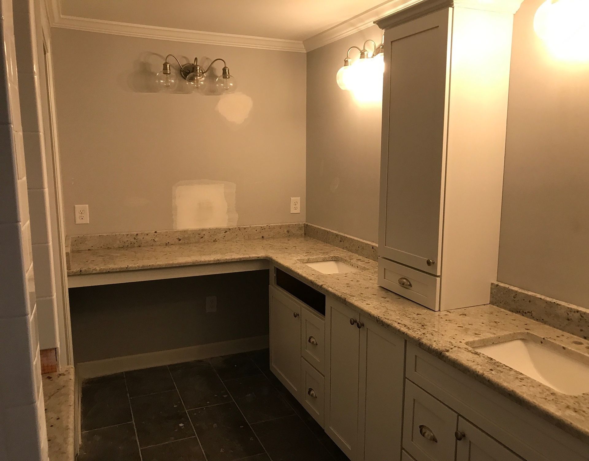 Empty kitchen with gray cabinets, speckled countertops, dark floor tiles, and bright wall lights