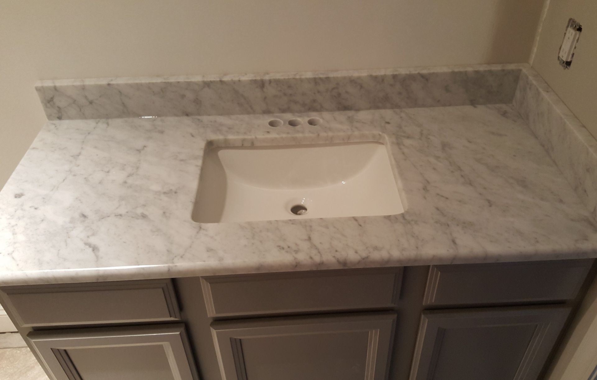 Marble bathroom vanity with a white undermount sink and gray cabinets under a beige wall and backsplash