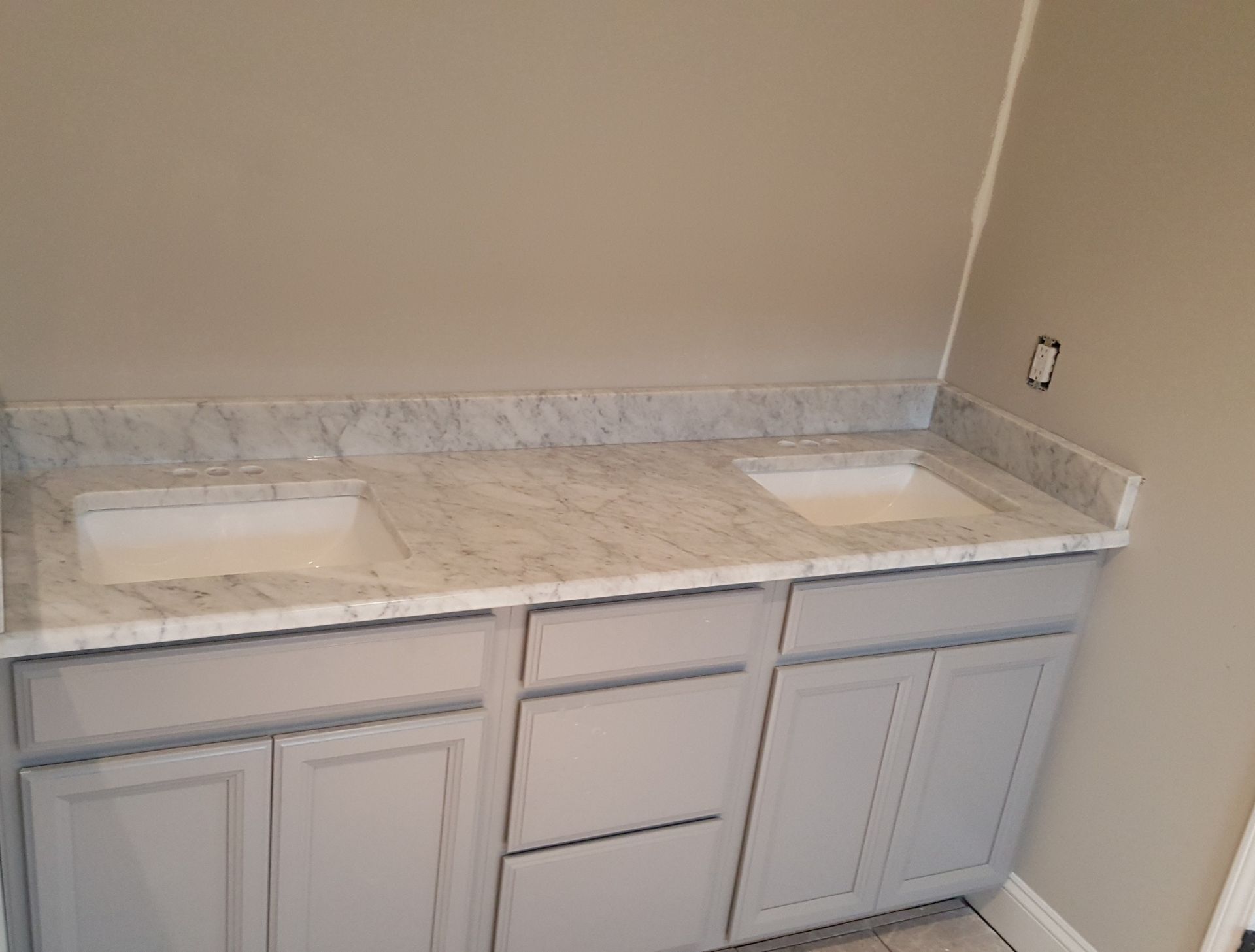 Double sink bathroom vanity with light stone countertop and gray cabinets, viewed in a corner.