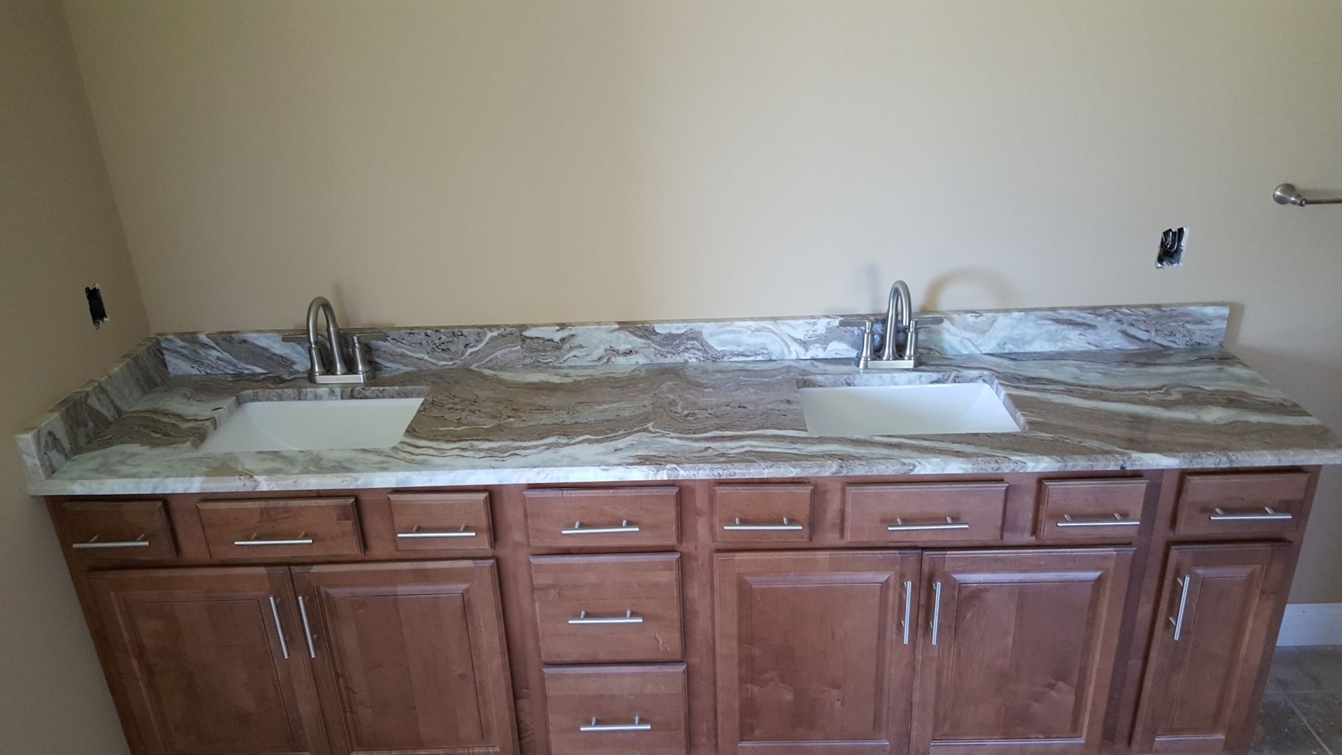 Double bathroom vanity with granite countertop, two sinks, wood cabinets, and a beige wall.