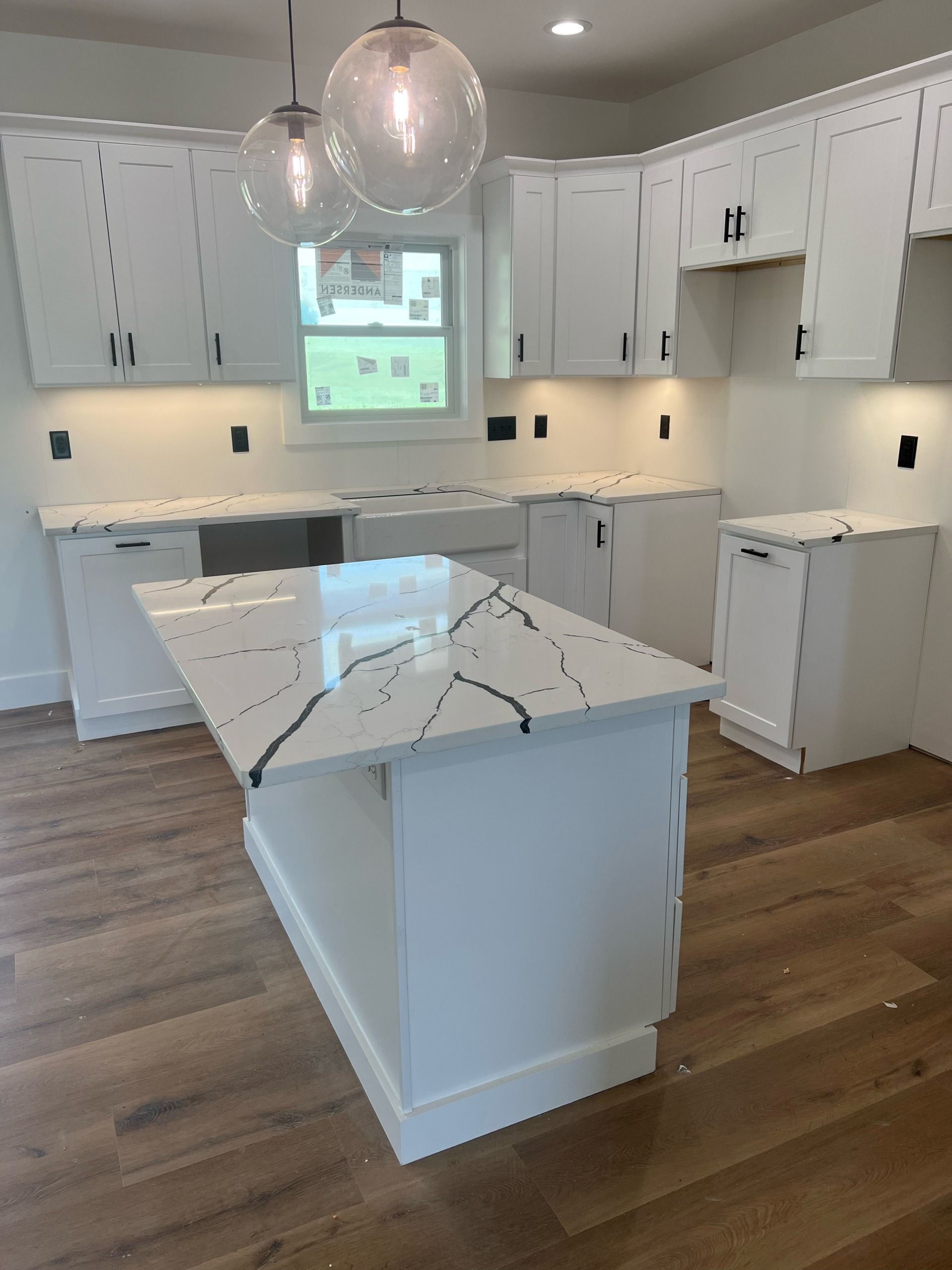 Bright white kitchen with marble island, pendant lights, and hardwood floors.