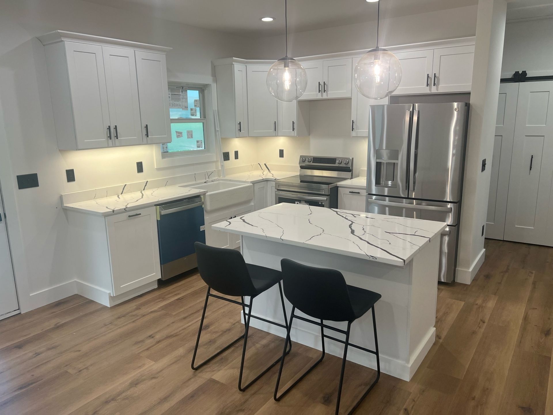 Modern white kitchen with marble island, stainless steel fridge, and two black stools on wood floors