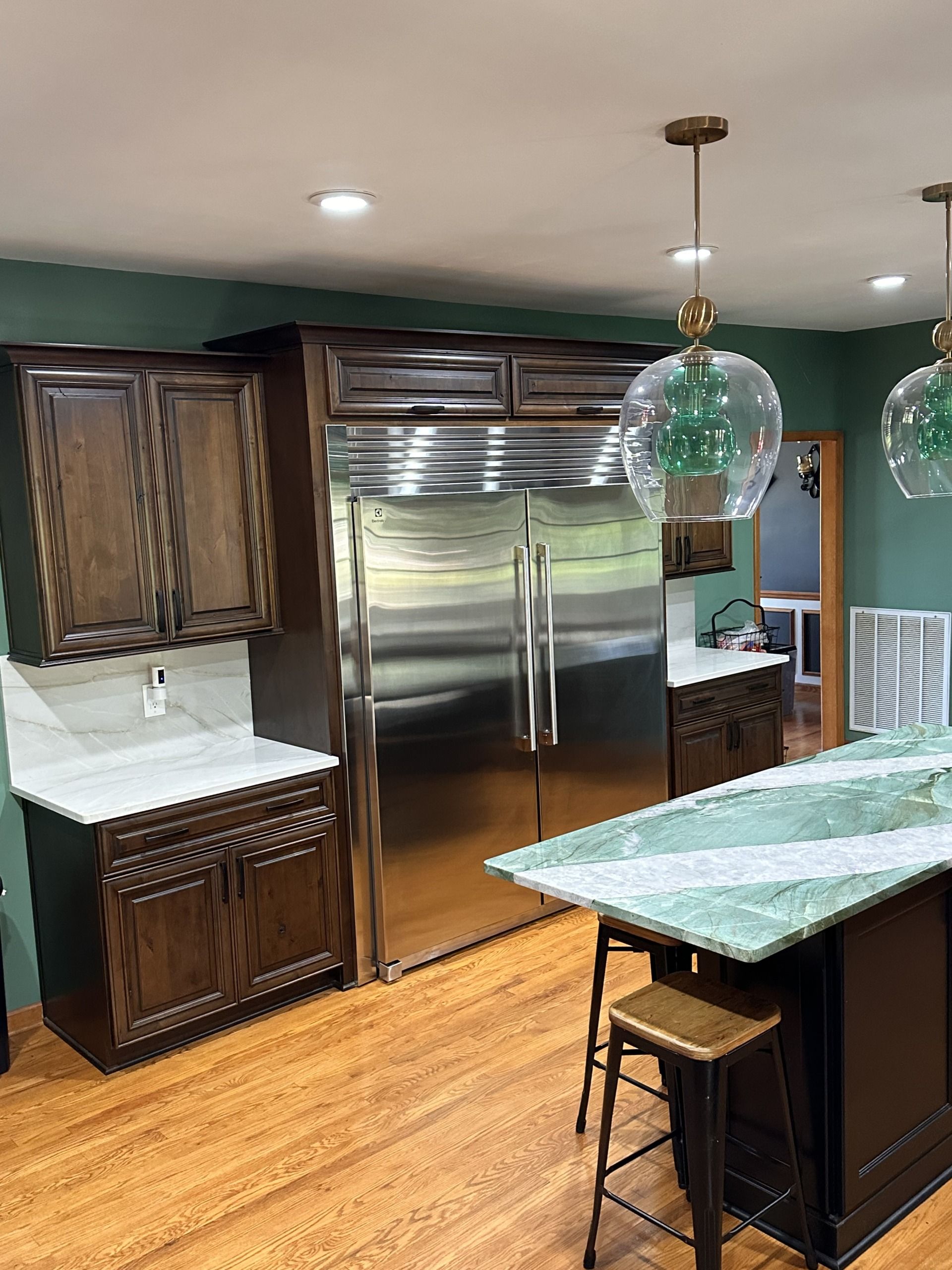 Modern kitchen with stainless steel fridge, dark wood cabinets, green island, and hanging glass pendant light