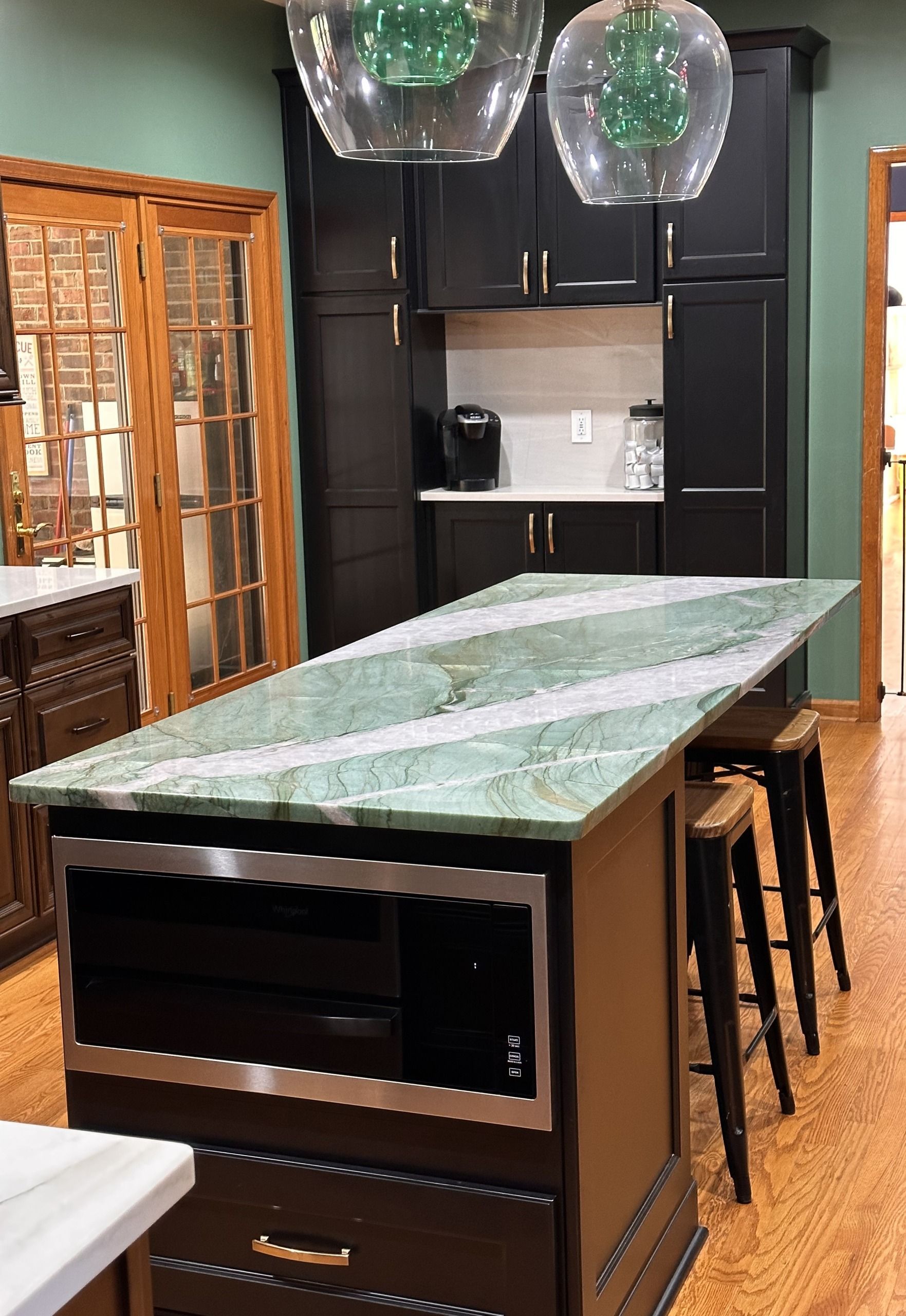 Modern kitchen with black cabinets, marble island, bar stools, and glass pendant lights
