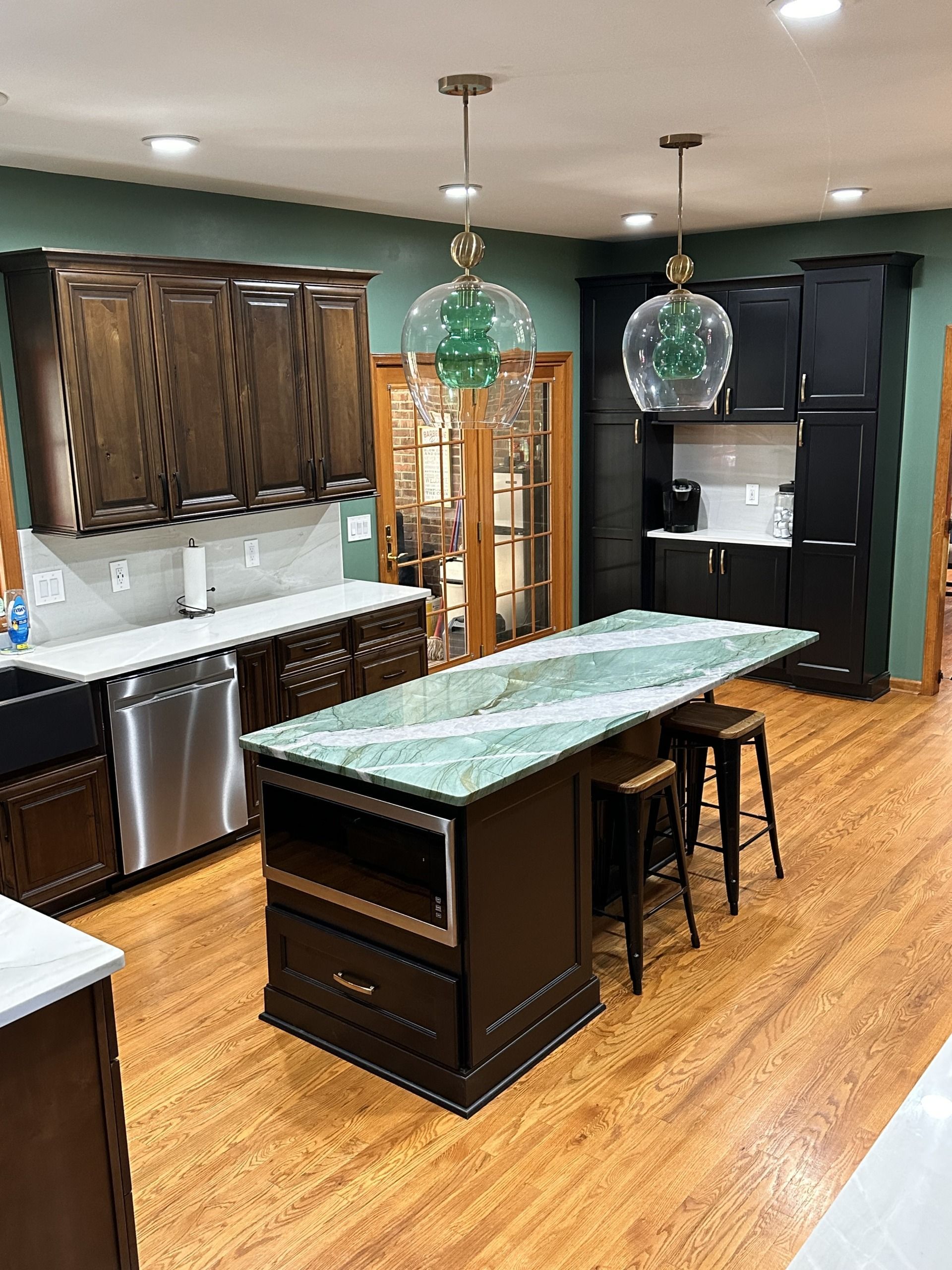 Modern kitchen with dark cabinets, green granite island, barstools, and hardwood floors.