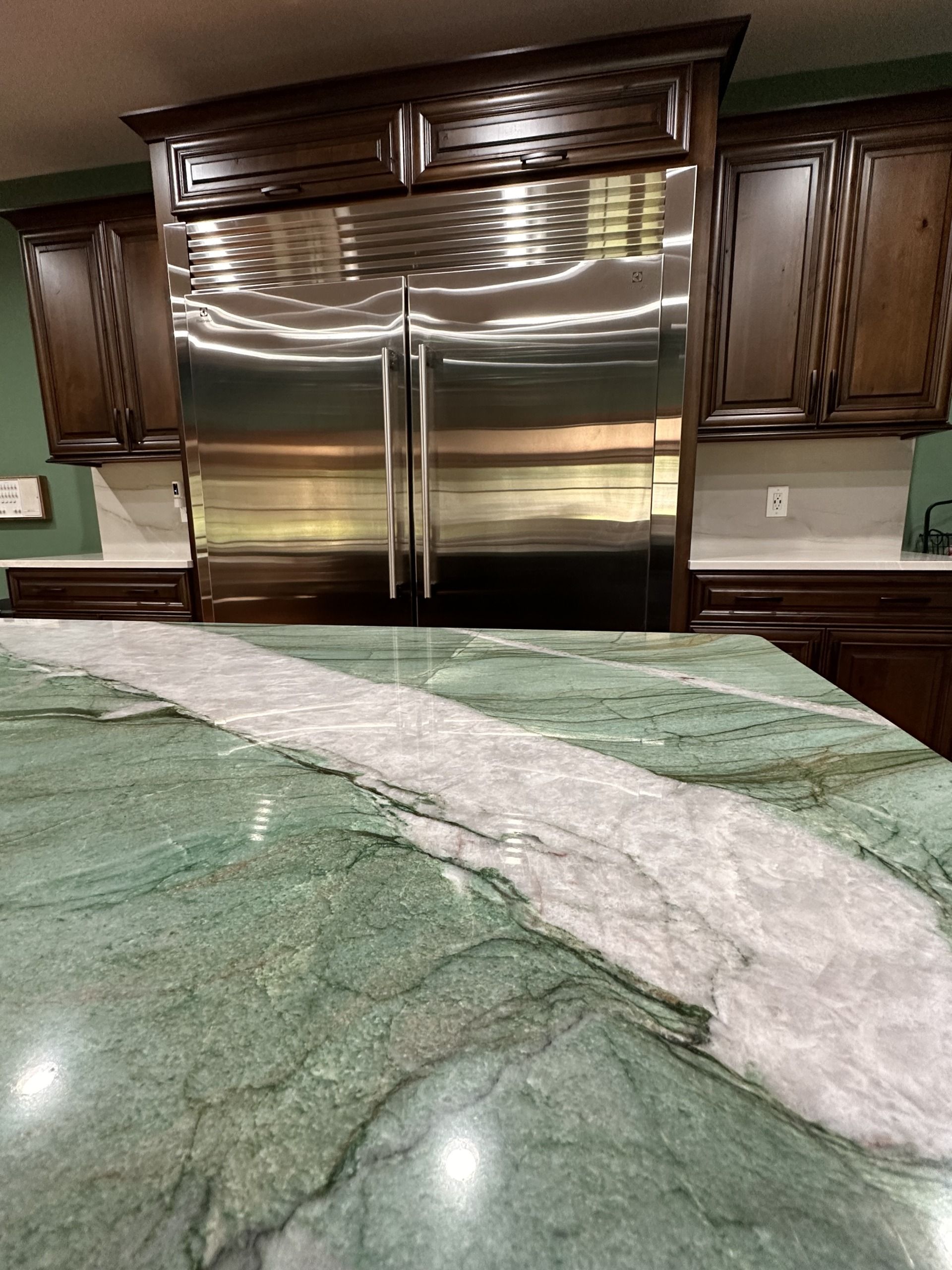 Kitchen with stainless steel double refrigerator, dark wood cabinets, and green granite island countertop