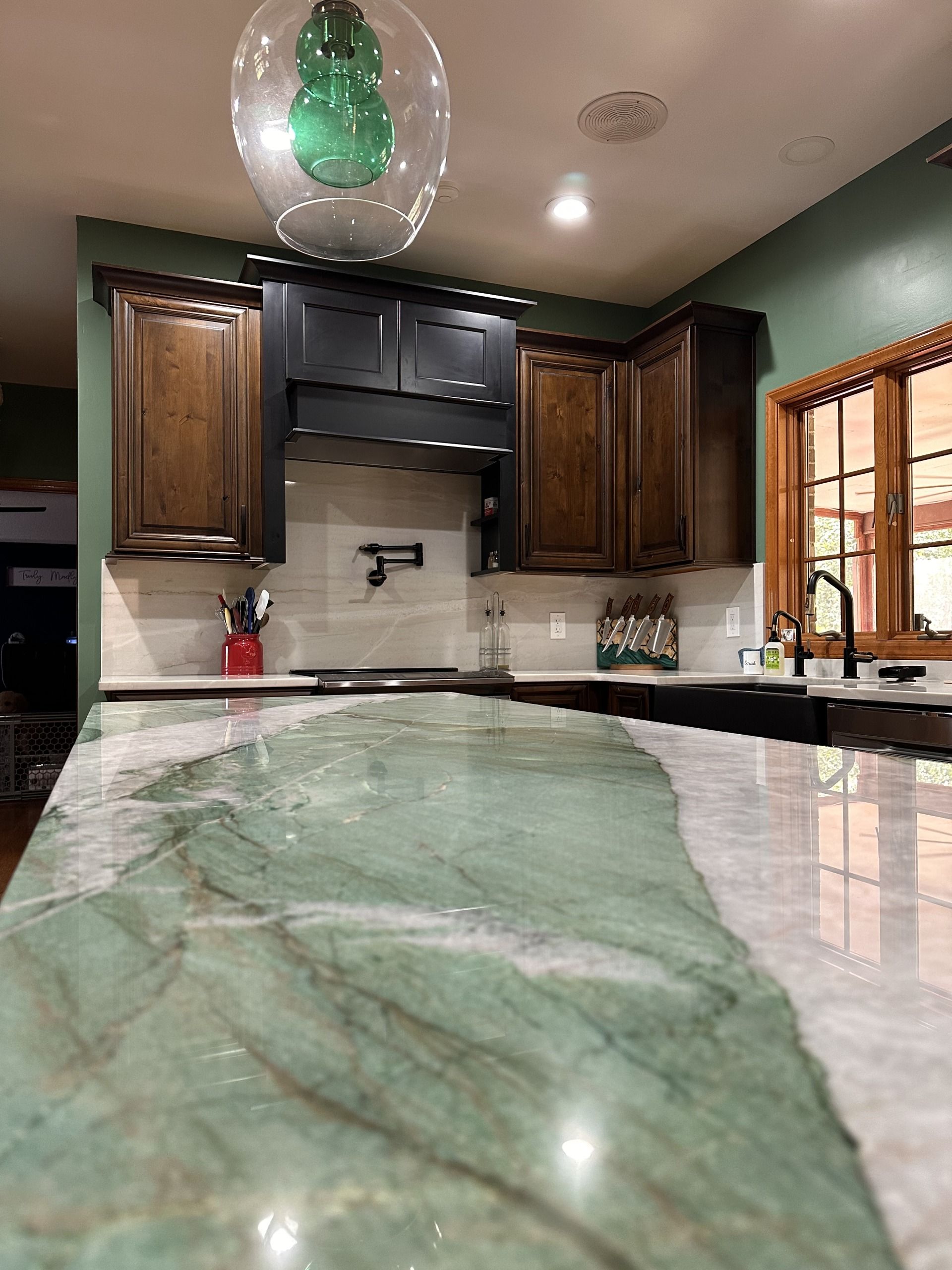 Kitchen with green marble island, dark wood cabinets, and a window over the sink.