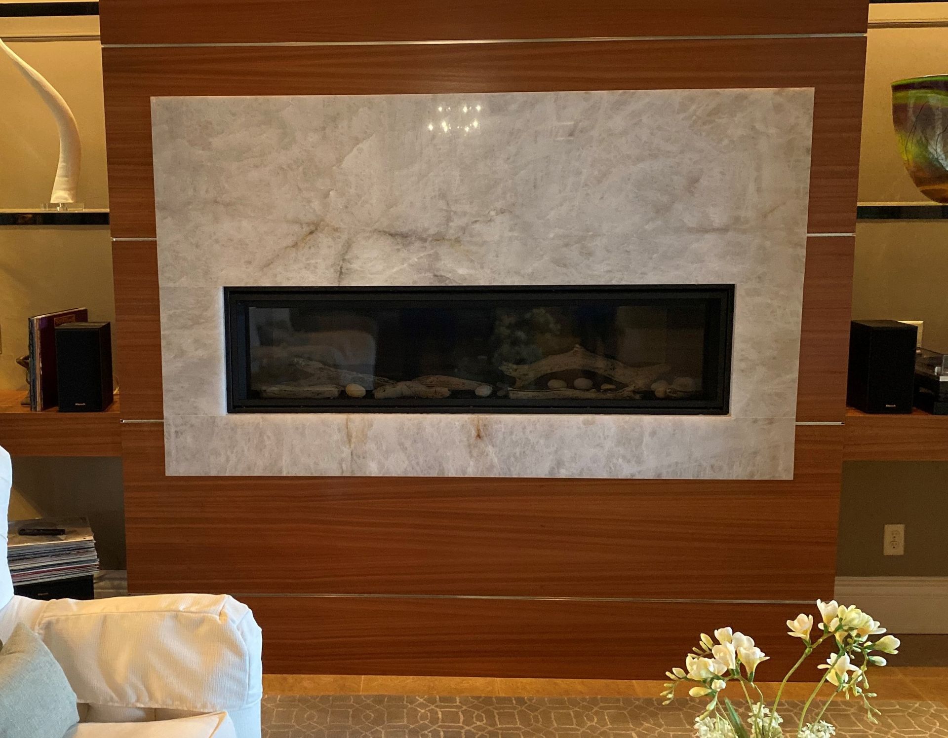 Modern fireplace with a long black firebox, framed by light stone and wood paneling in a living room.