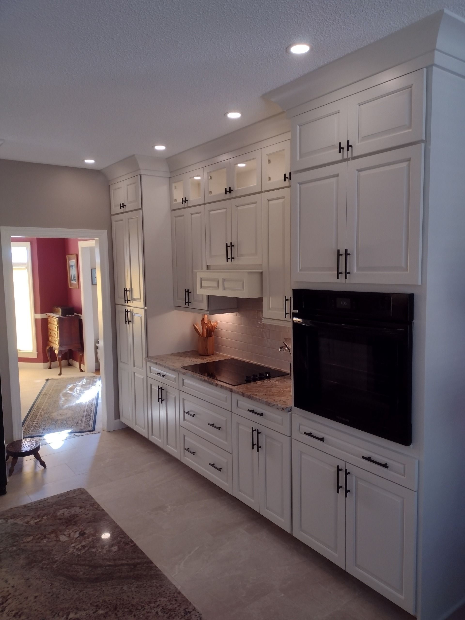 Bright modern kitchen with white cabinets, built-in oven, granite countertops, and recessed lighting