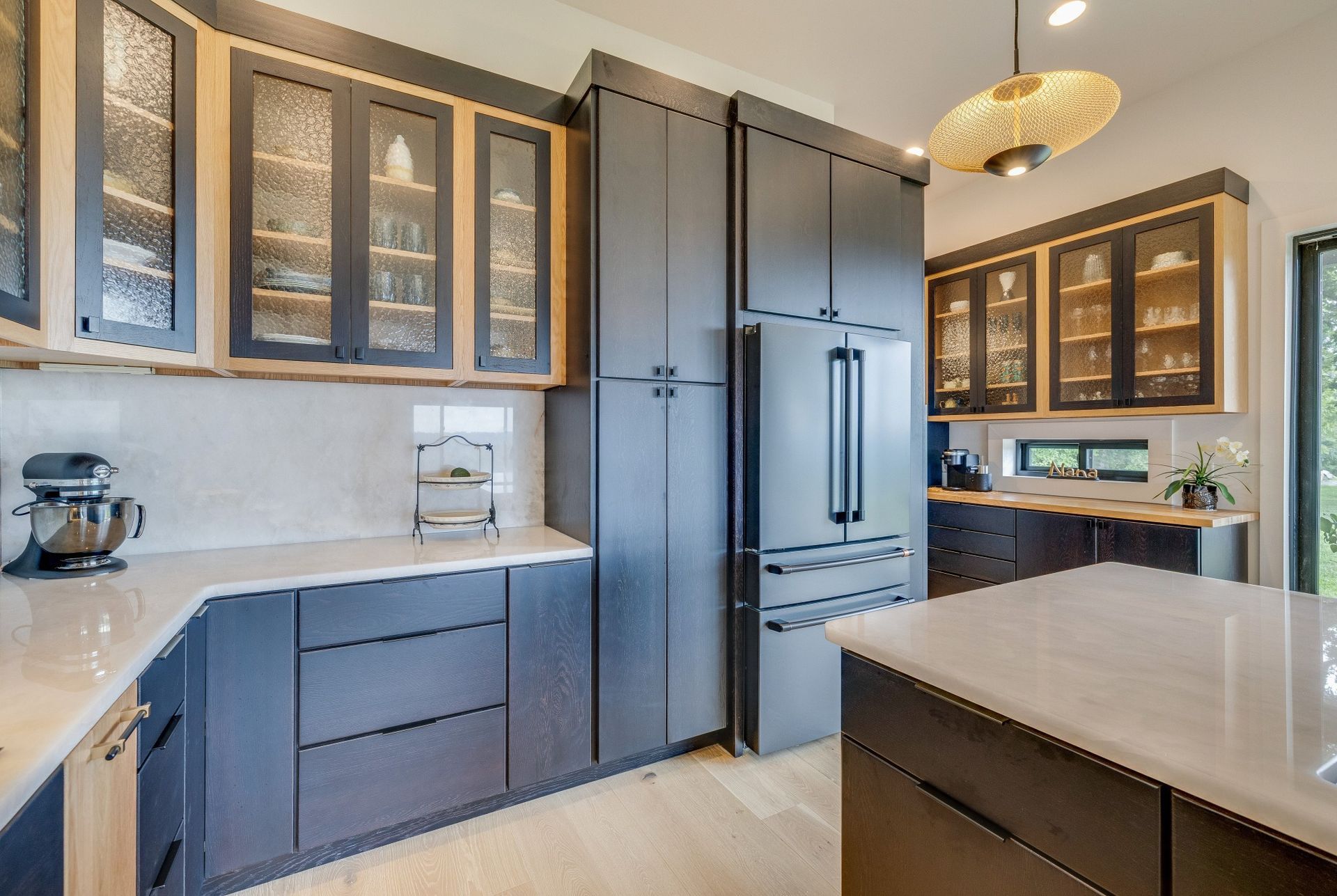 Modern kitchen with gray cabinets, stainless steel fridge, and large island under pendant light