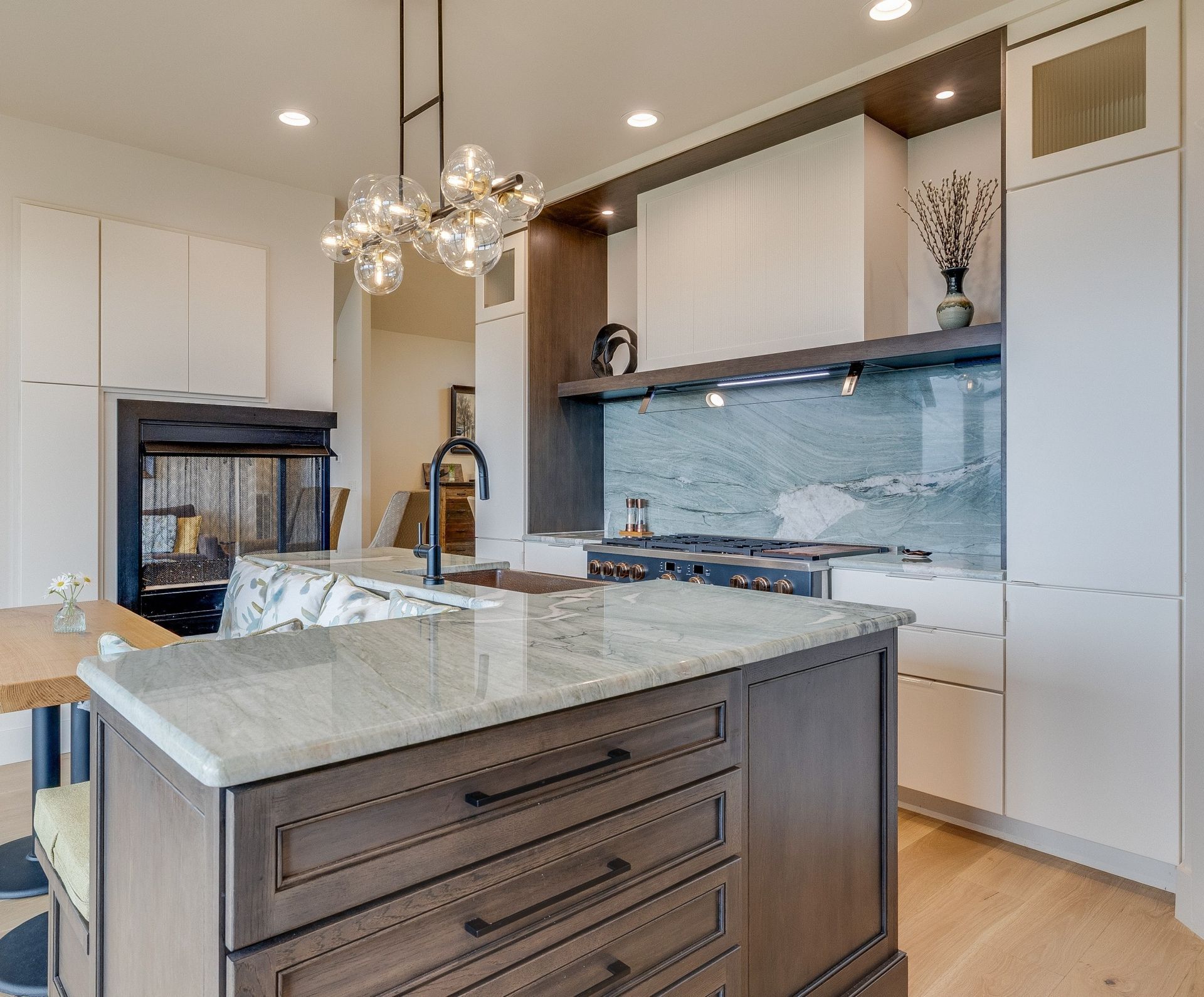 Modern kitchen with marble island, white cabinets, blue tile backsplash, and pendant chandelier