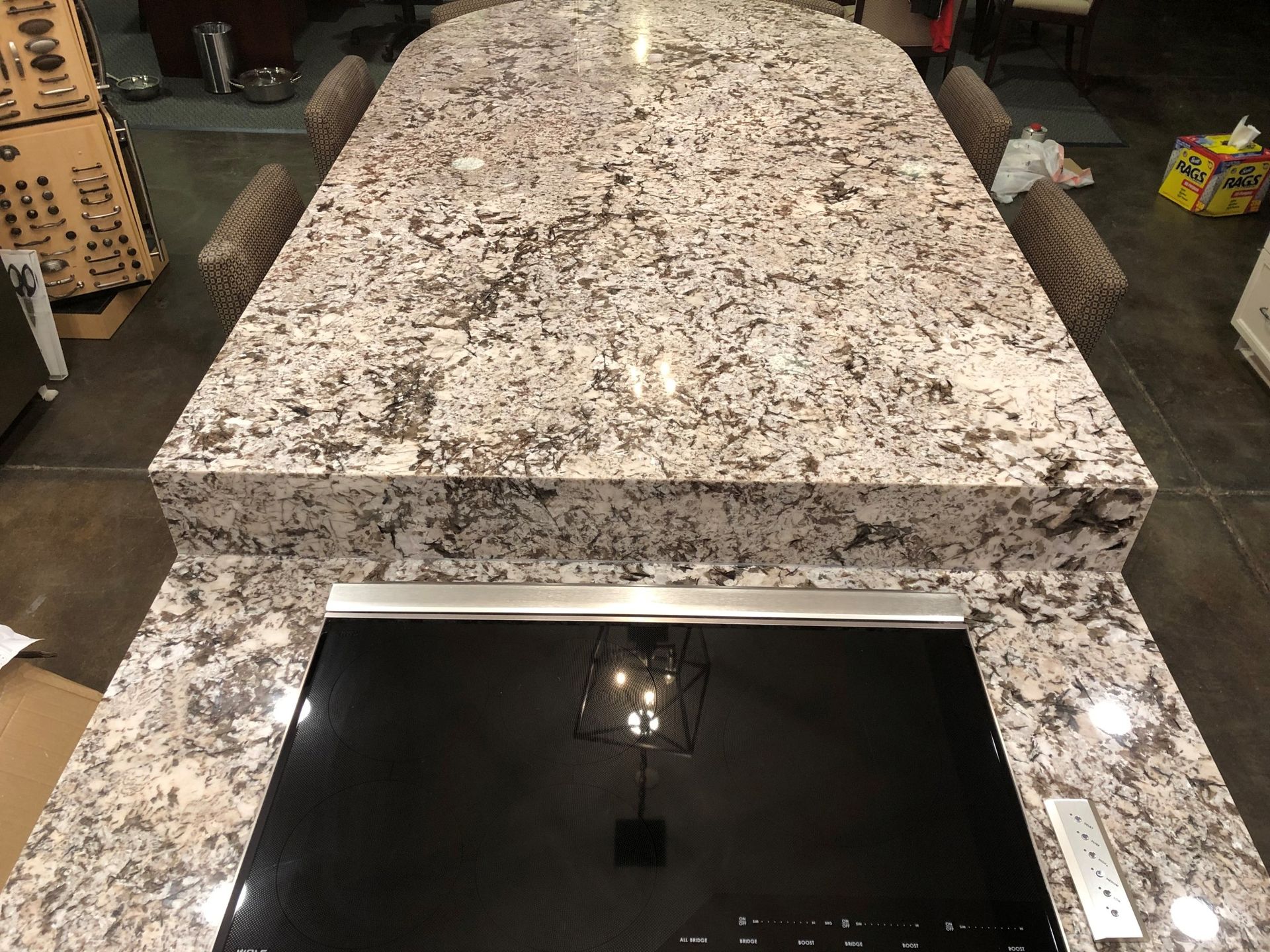 White-and-speckled granite kitchen island with a black glass cooktop in a dimly lit kitchen.