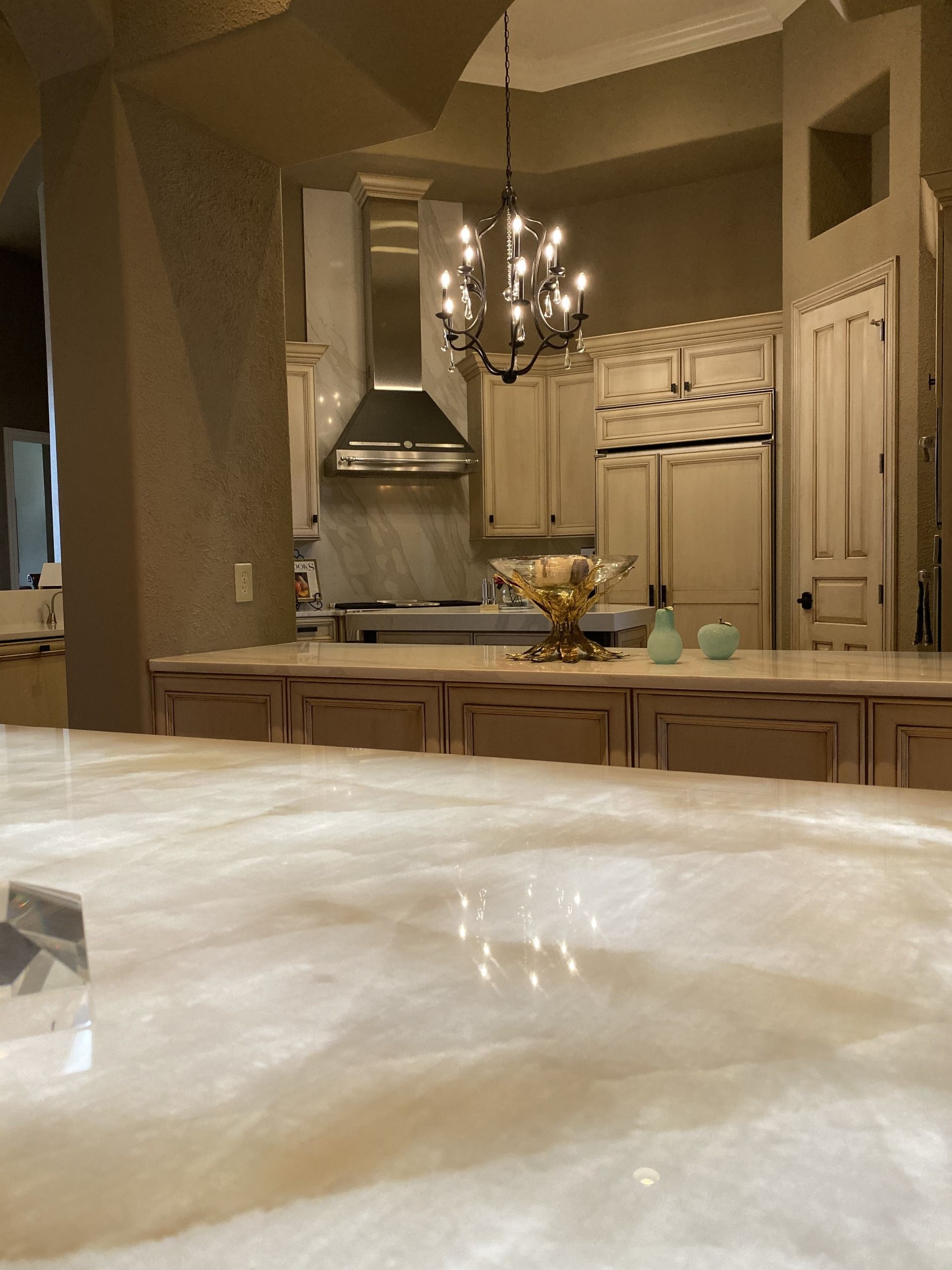 Warm kitchen with cream cabinets, chandelier, island, and a countertop in the foreground.