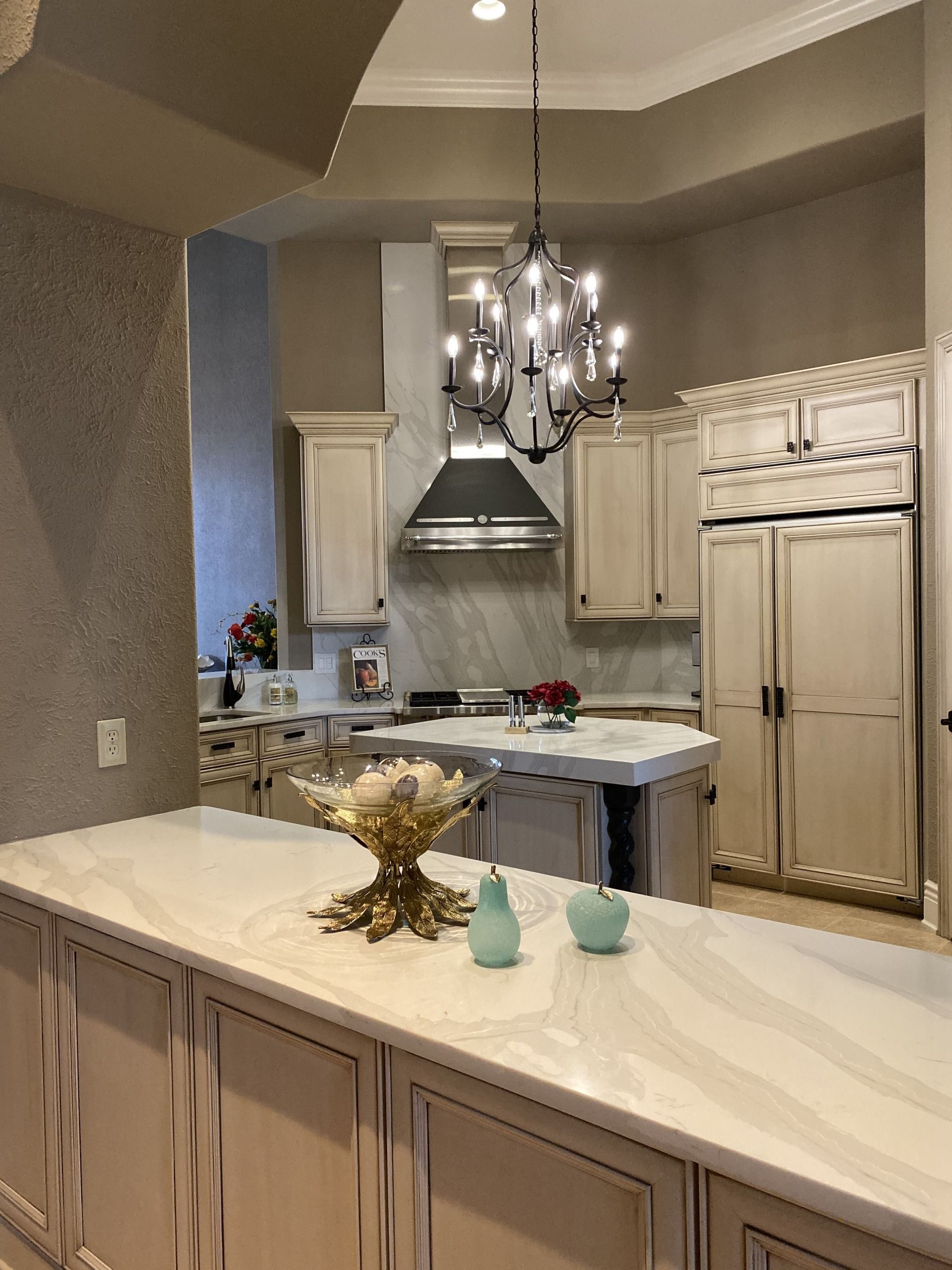 Modern kitchen with white cabinets, marble island, chandelier, and stainless steel range hood