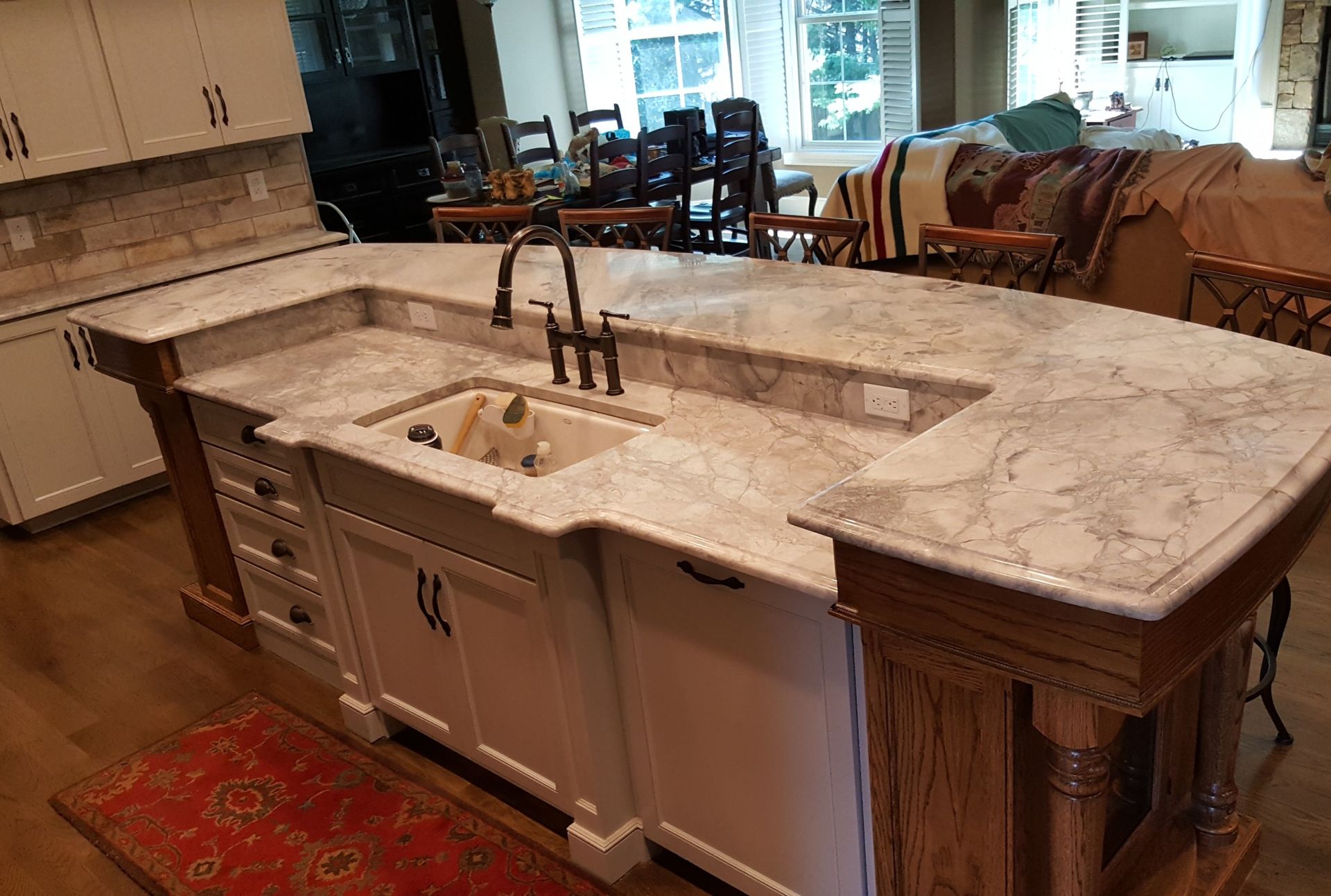 Luxury kitchen island with marble countertop, built-in sink, and brass faucet in a bright open interior