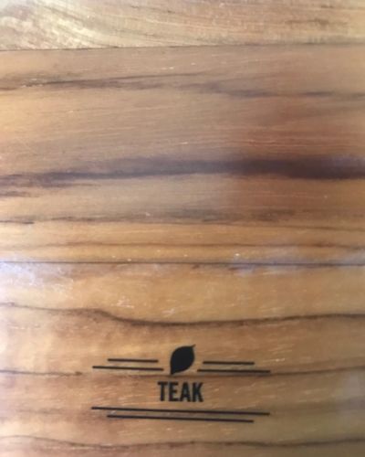 Close-up of a teak wood grain surface with a small “TEAK” label near the center.