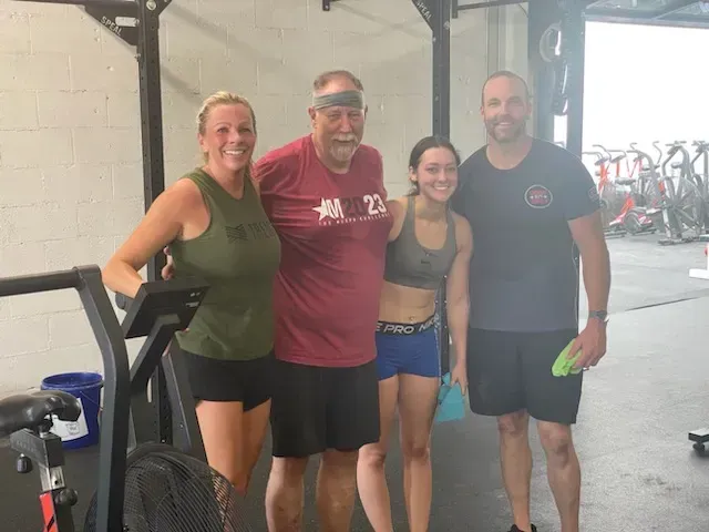 Four gym-goers pose smiling at CrossFit Exile, with bikes and workout equipment in the background.