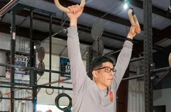 Person doing a pull-up in a gym, arms extended overhead on gymnastic rings at CrossFit Exile.