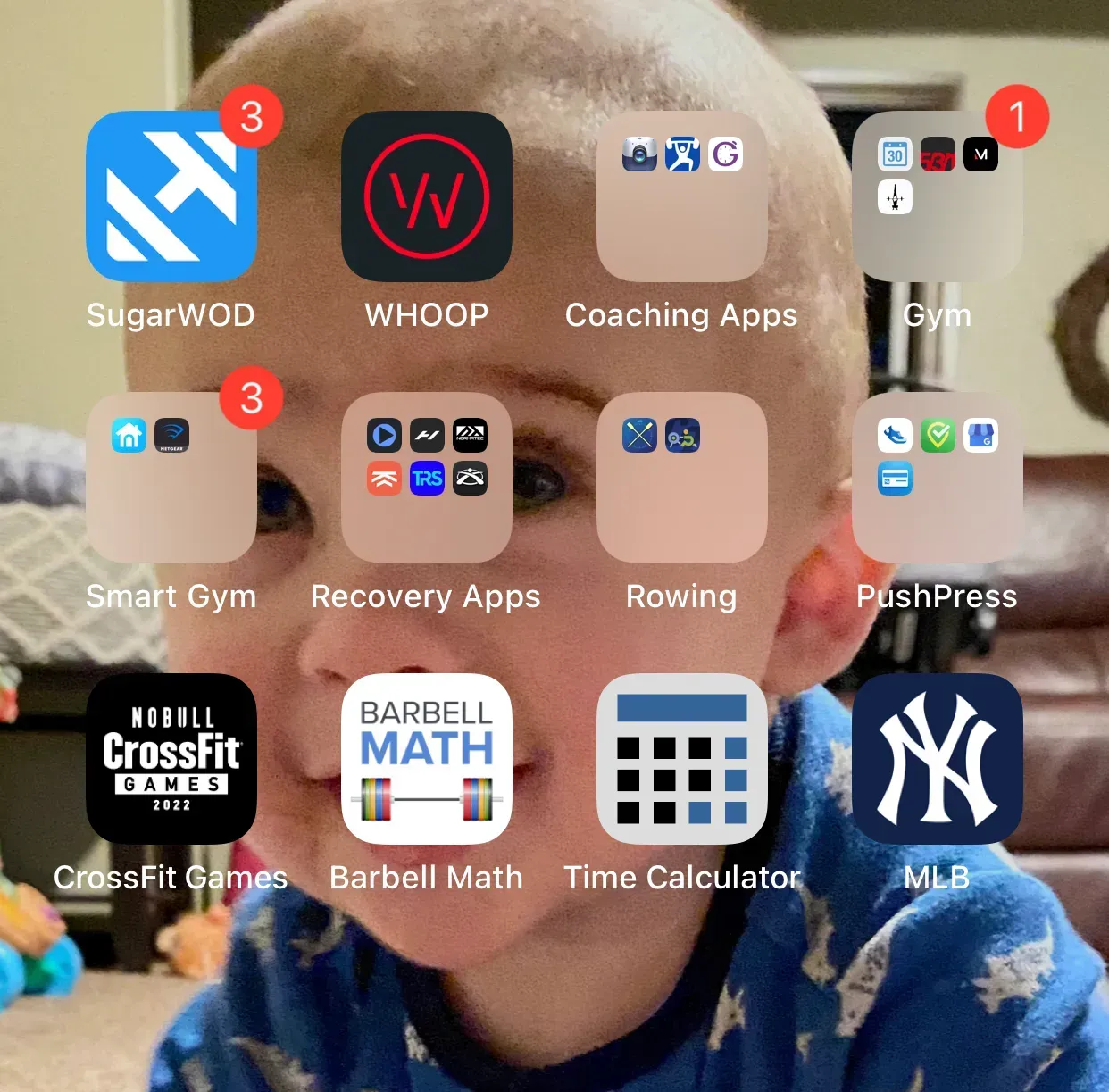 Smartphone home screen with fitness app folders over a child’s smiling face wallpaper