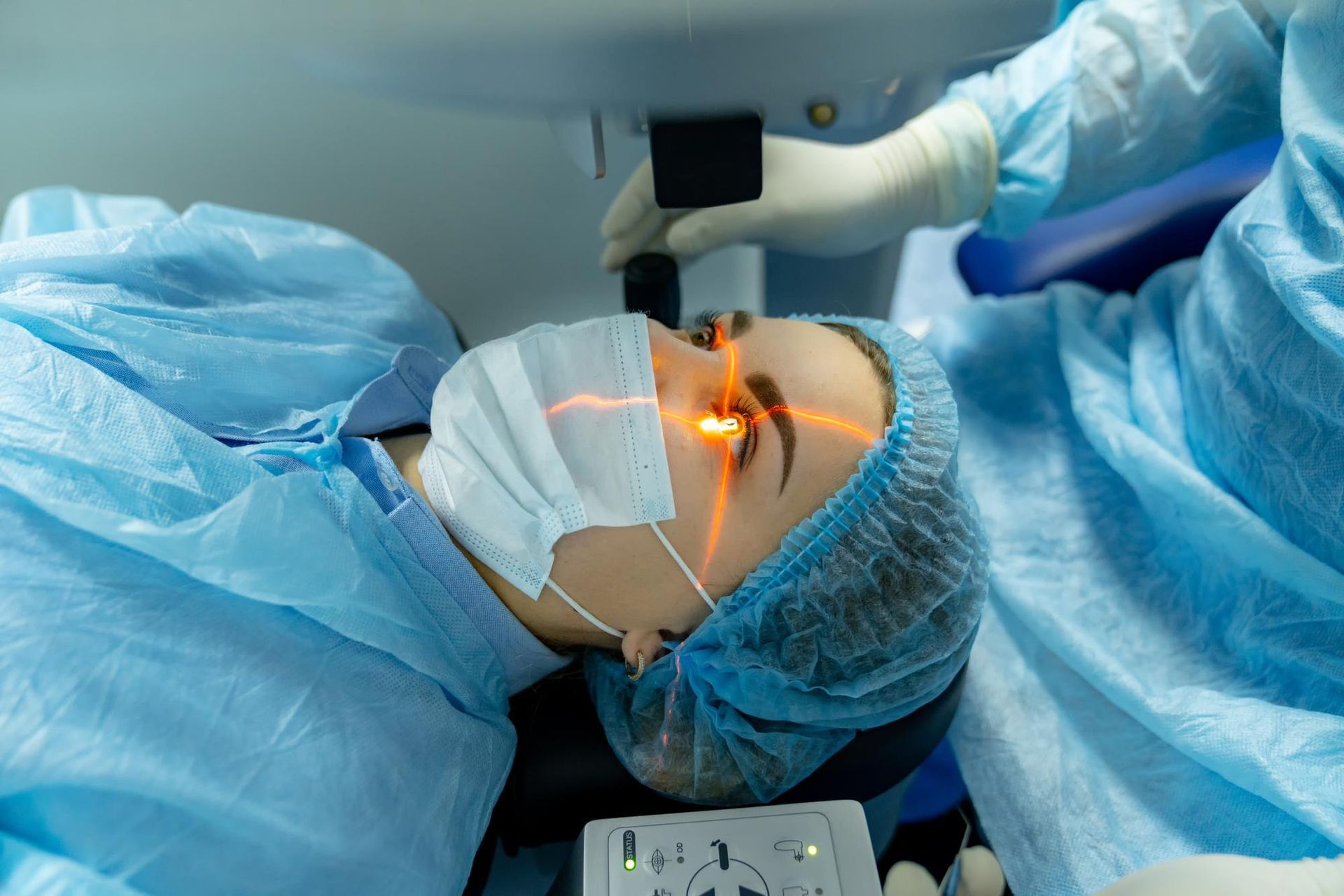 Person undergoing eye surgery with laser; orange light directed at eye, surgical setting.