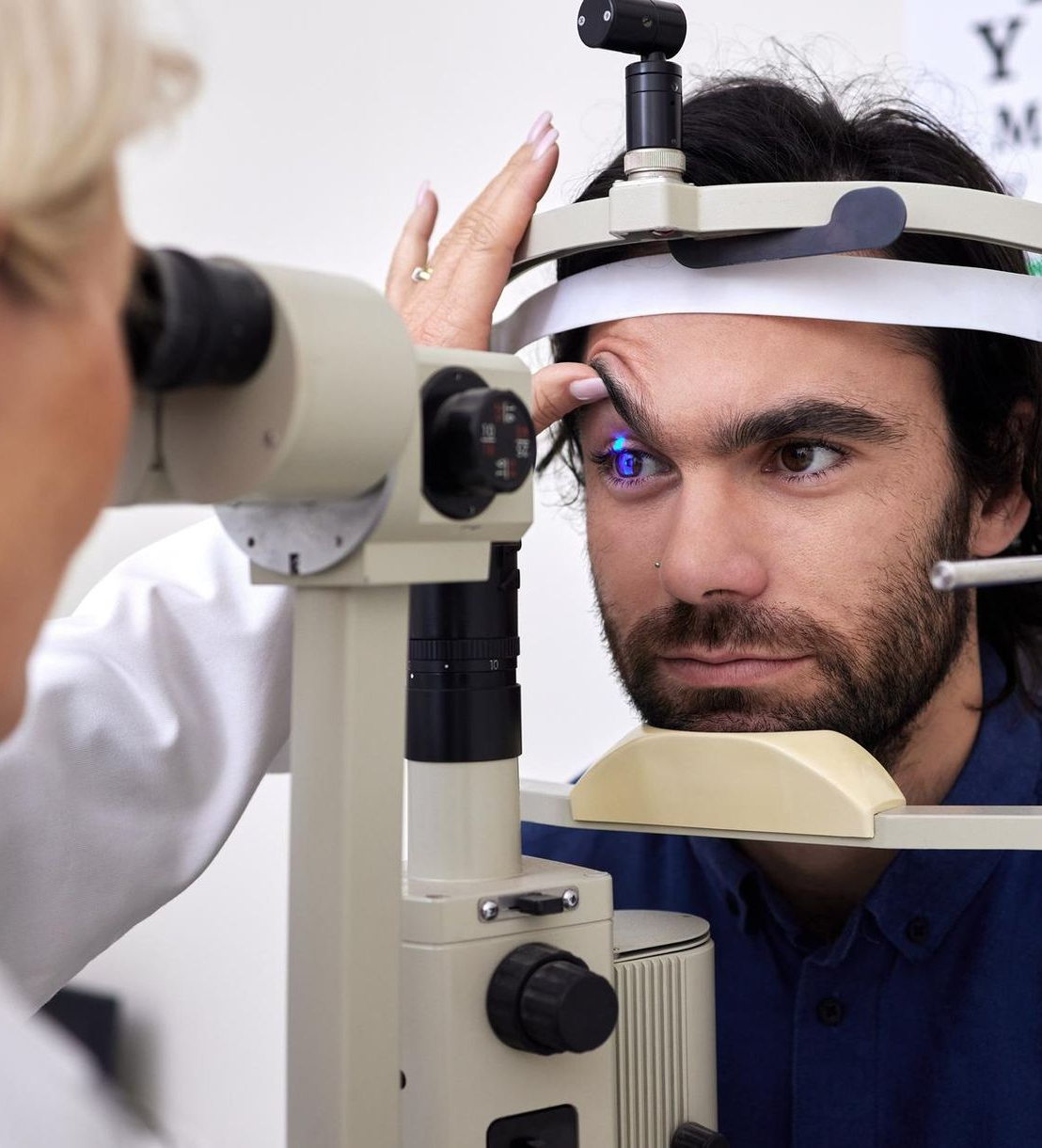 Optometrist examining a man's eye with a slit lamp. The man looks forward, a blue light shines.