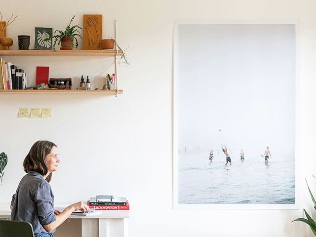 A woman is sitting at a desk in front of a large picture of people in the ocean.