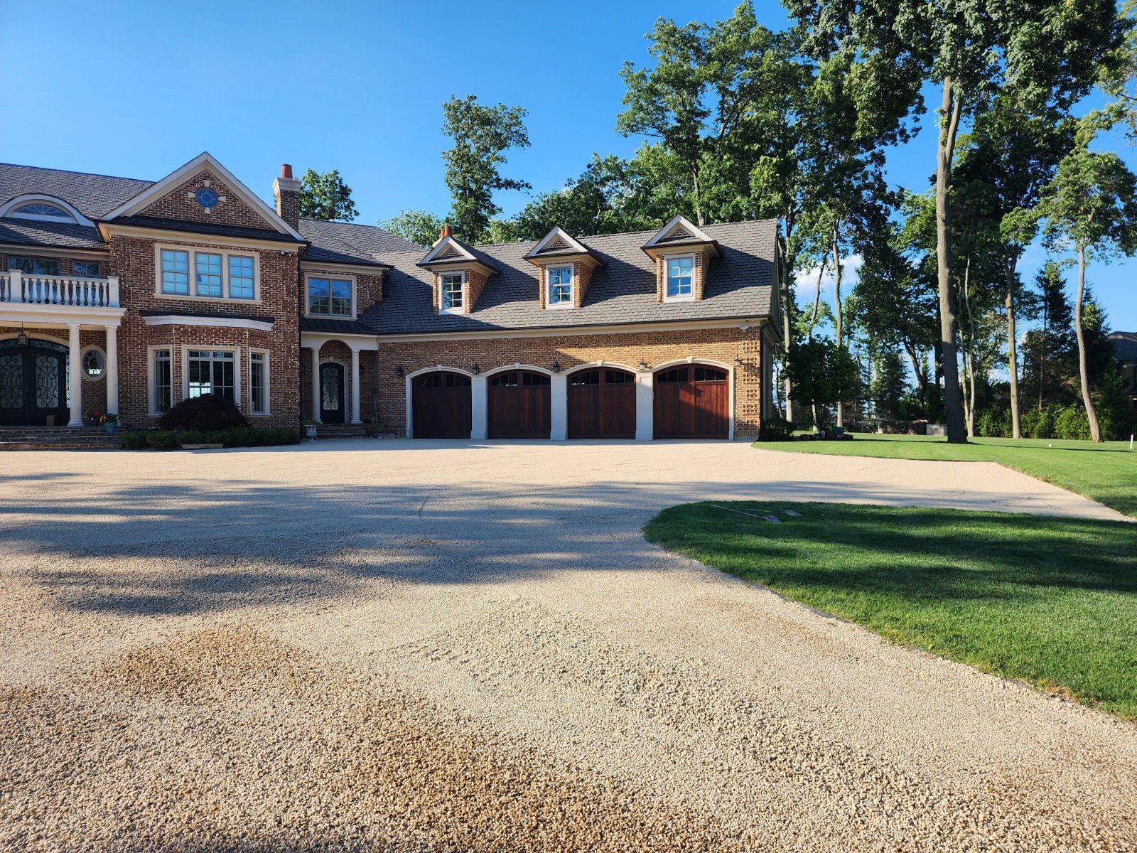 A large, multi-story brick house with a four-car garage and a wide gravel driveway on a sunny day.