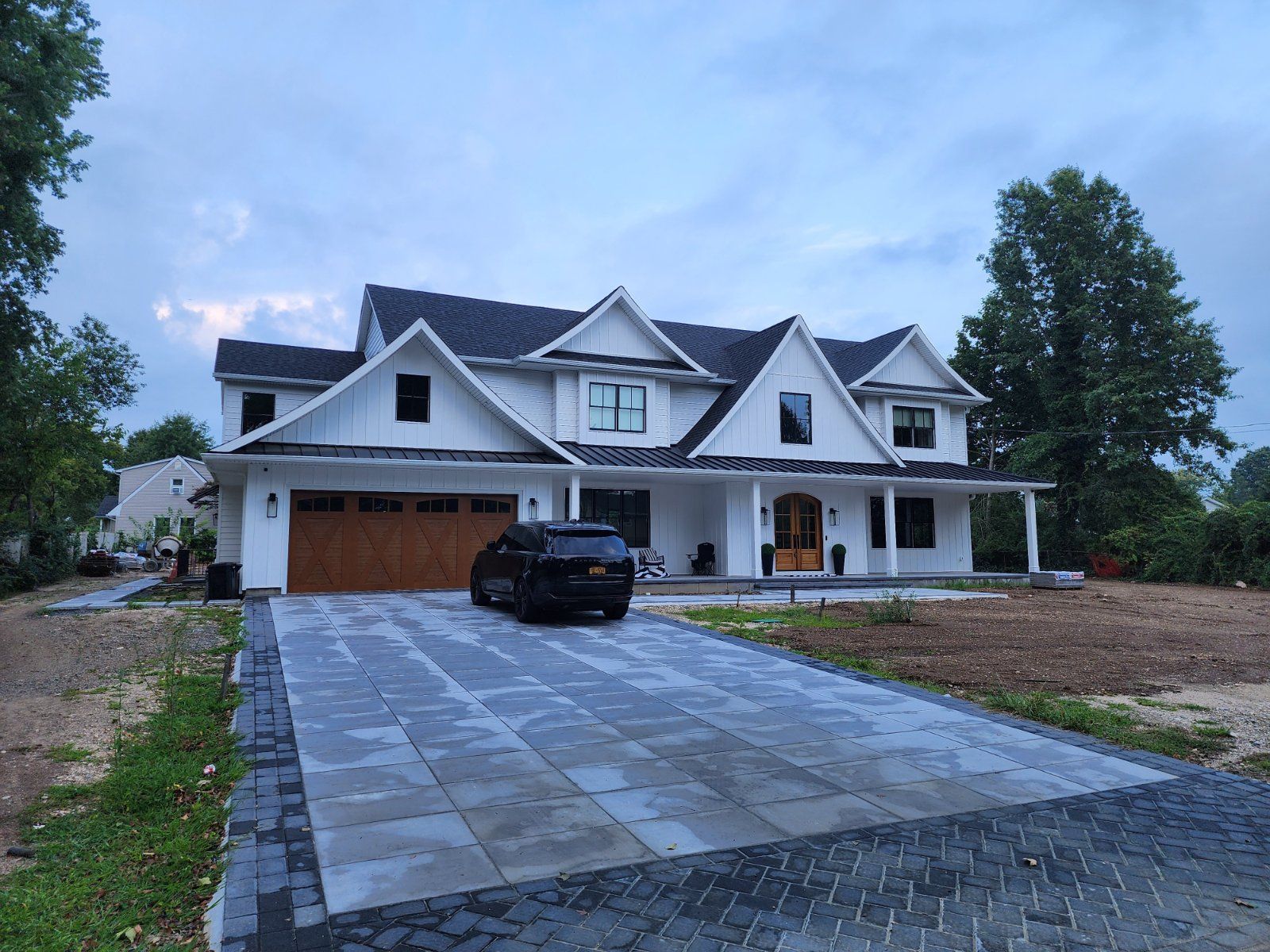 A newly built, two-story white house with a dark roof and wooden garage door, featuring a paved driveway and a parked car.