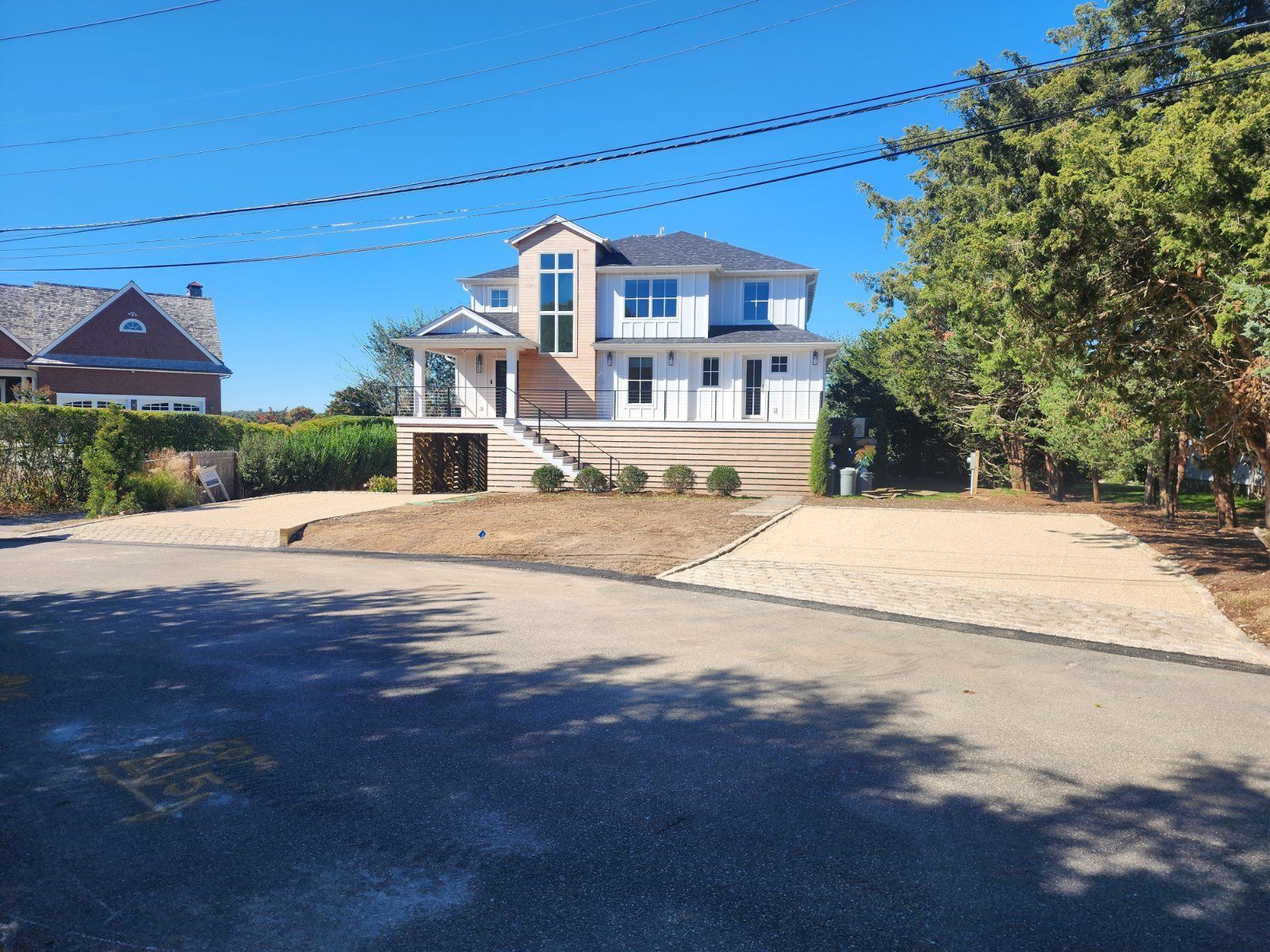 A two-story, modern white house with a paved driveway and landscaped front yard under a clear blue sky.
