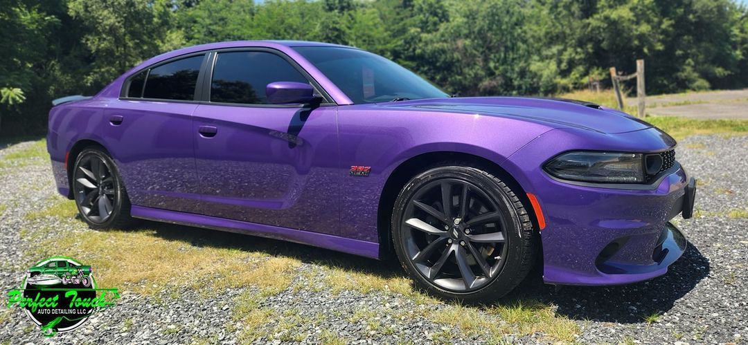 A purple dodge charger is parked in a gravel lot.