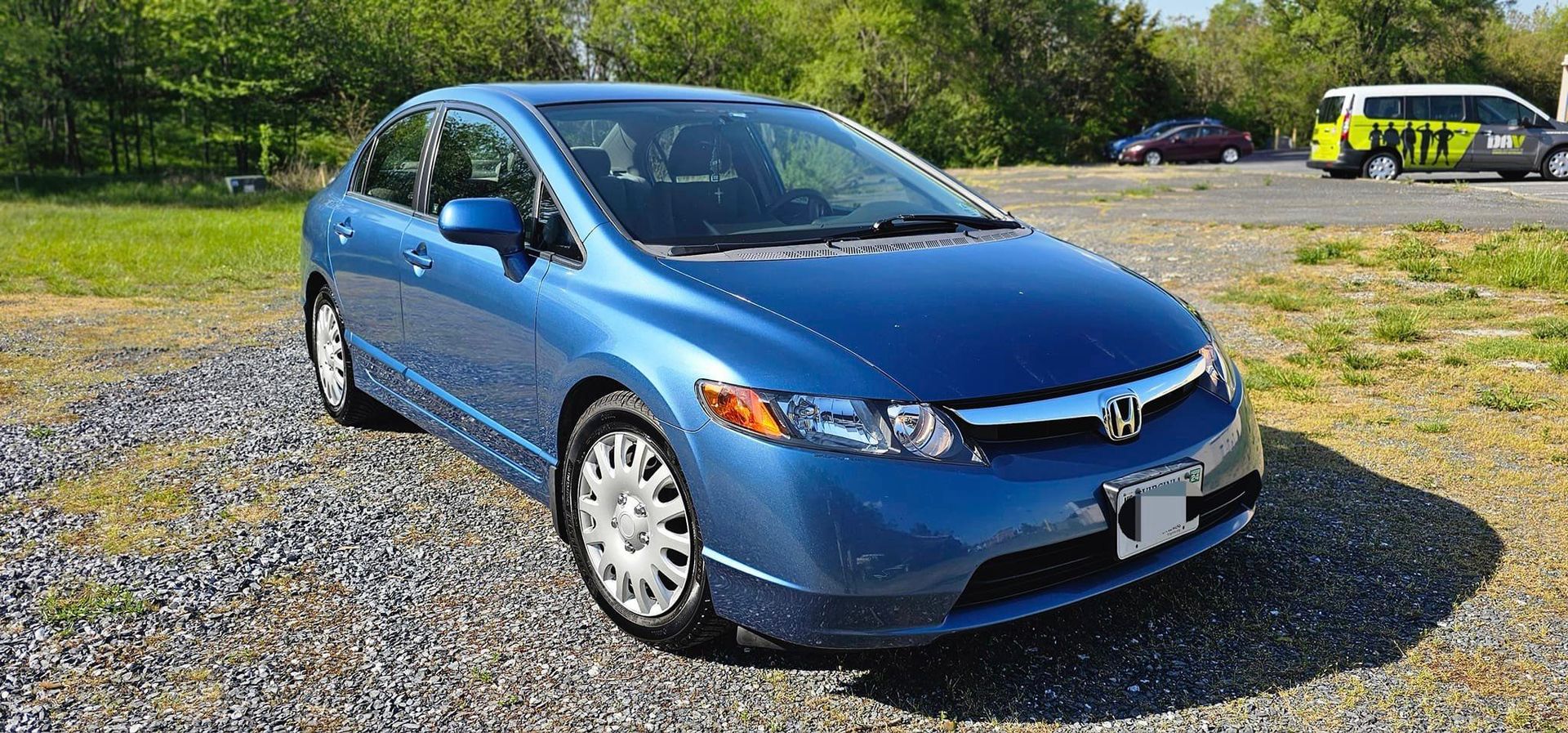 A blue honda civic is parked in a gravel lot.