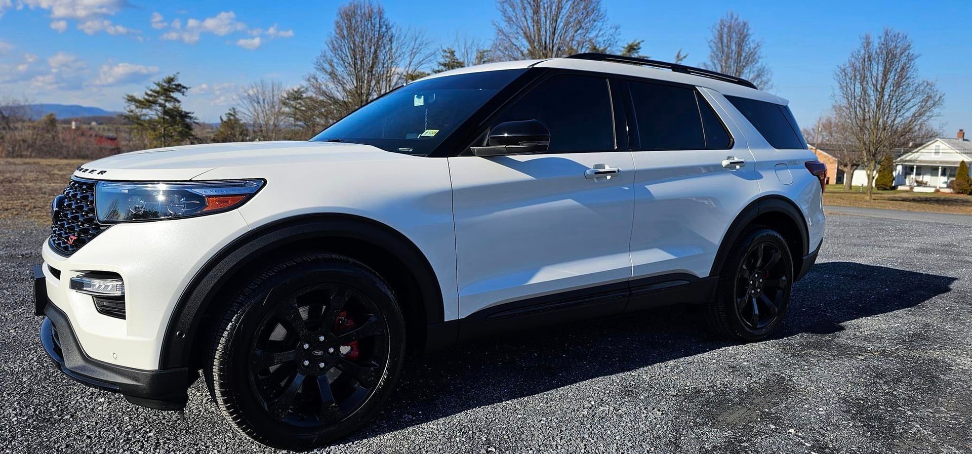 A white ford explorer is parked in a gravel lot.