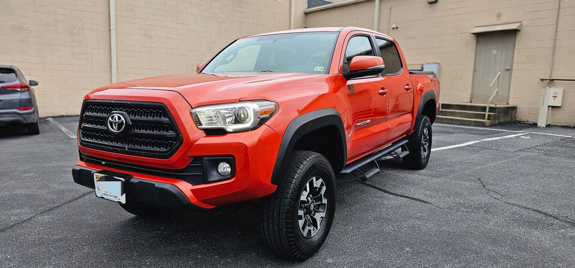 A red toyota tacoma truck is parked in a parking lot in front of a building.