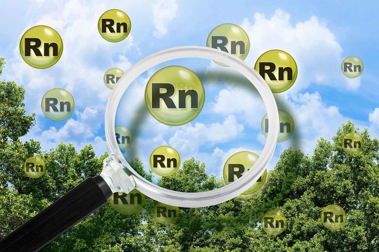 Magnifying glass over floating radon symbols (Rn) against a sky and trees.