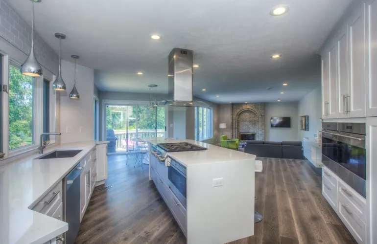 Modern kitchen with white cabinets, island with cooktop, and open concept to living area.