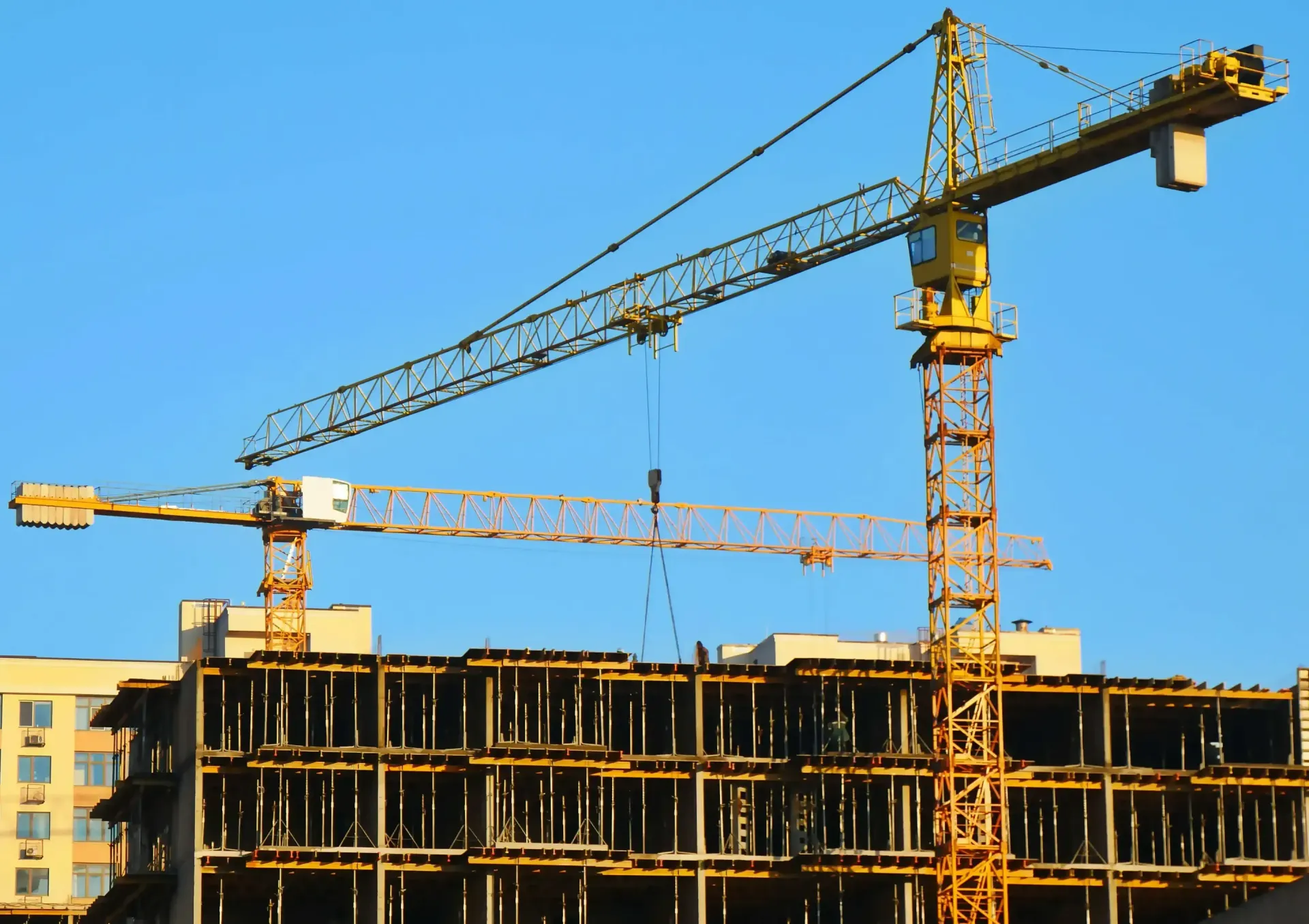 Two yellow construction cranes over a building under construction, against a clear blue sky.