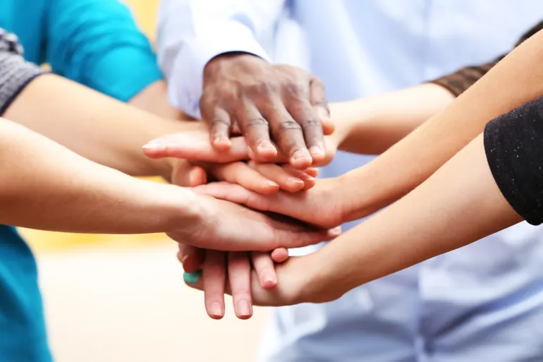 Hands of various skin tones stacked in a group huddle, teamwork and unity.