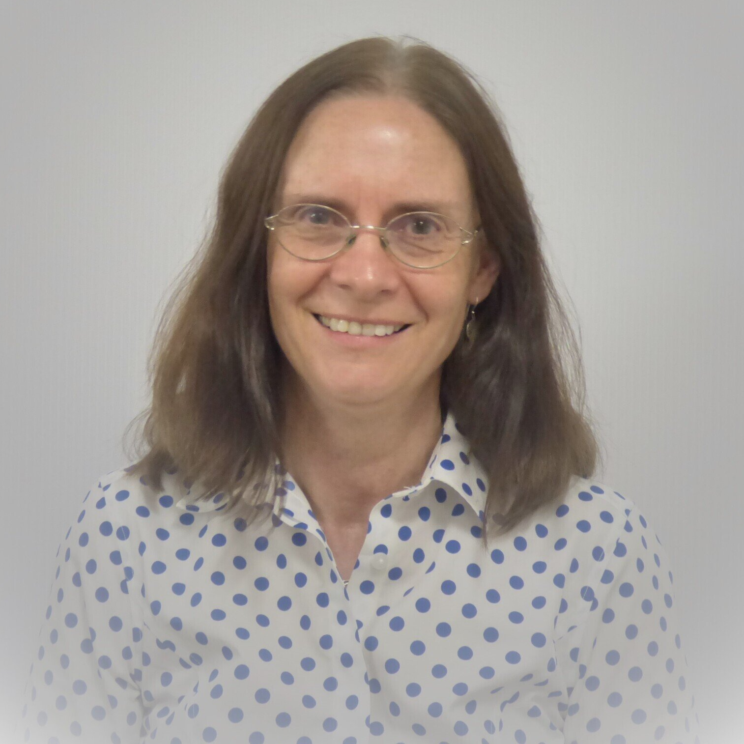 A woman wearing glasses and a polka dot shirt smiles for the camera