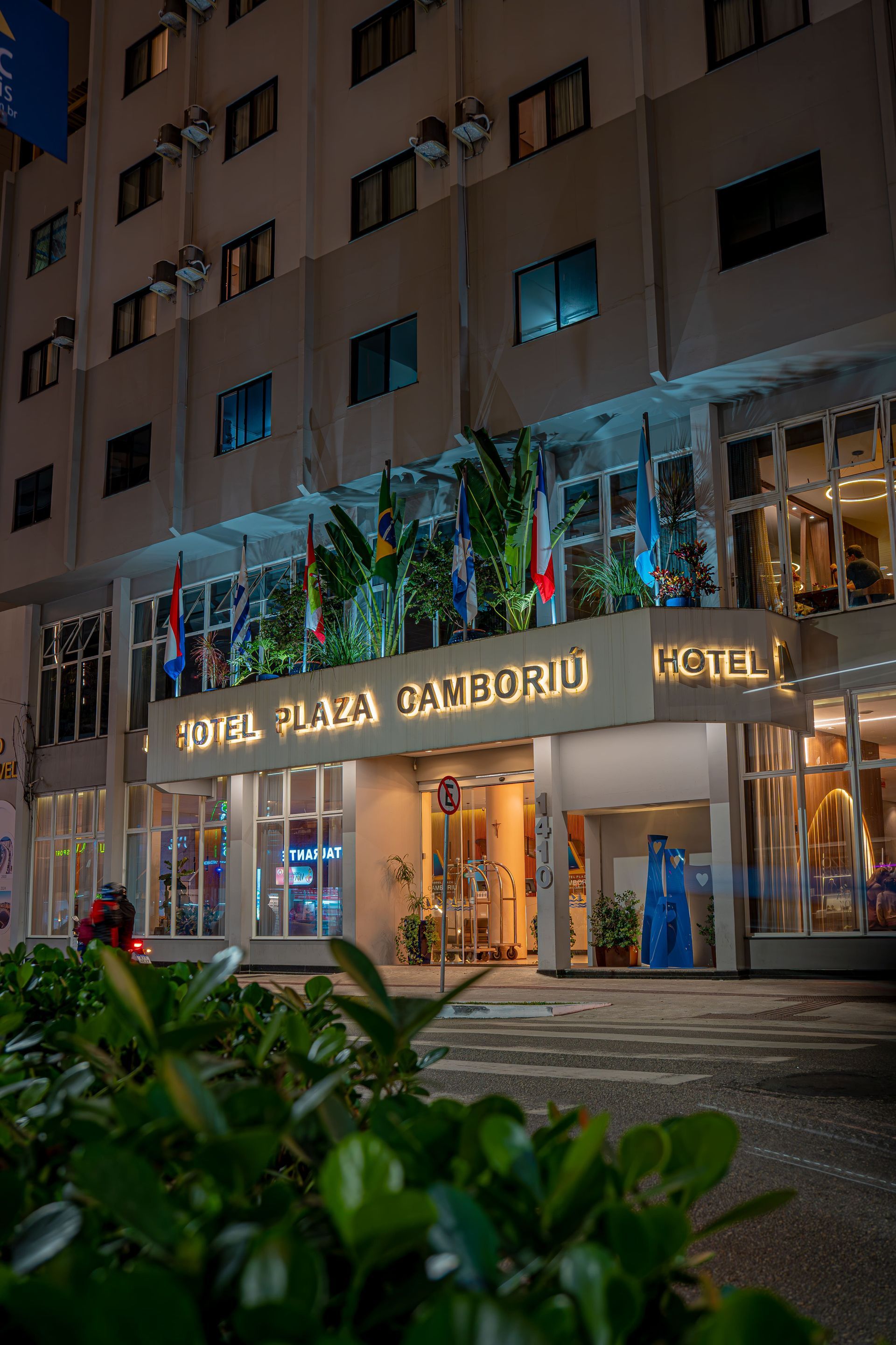 Exterior do Hotel Plaza Camboriú, um prédio alto e branco com bandeiras.