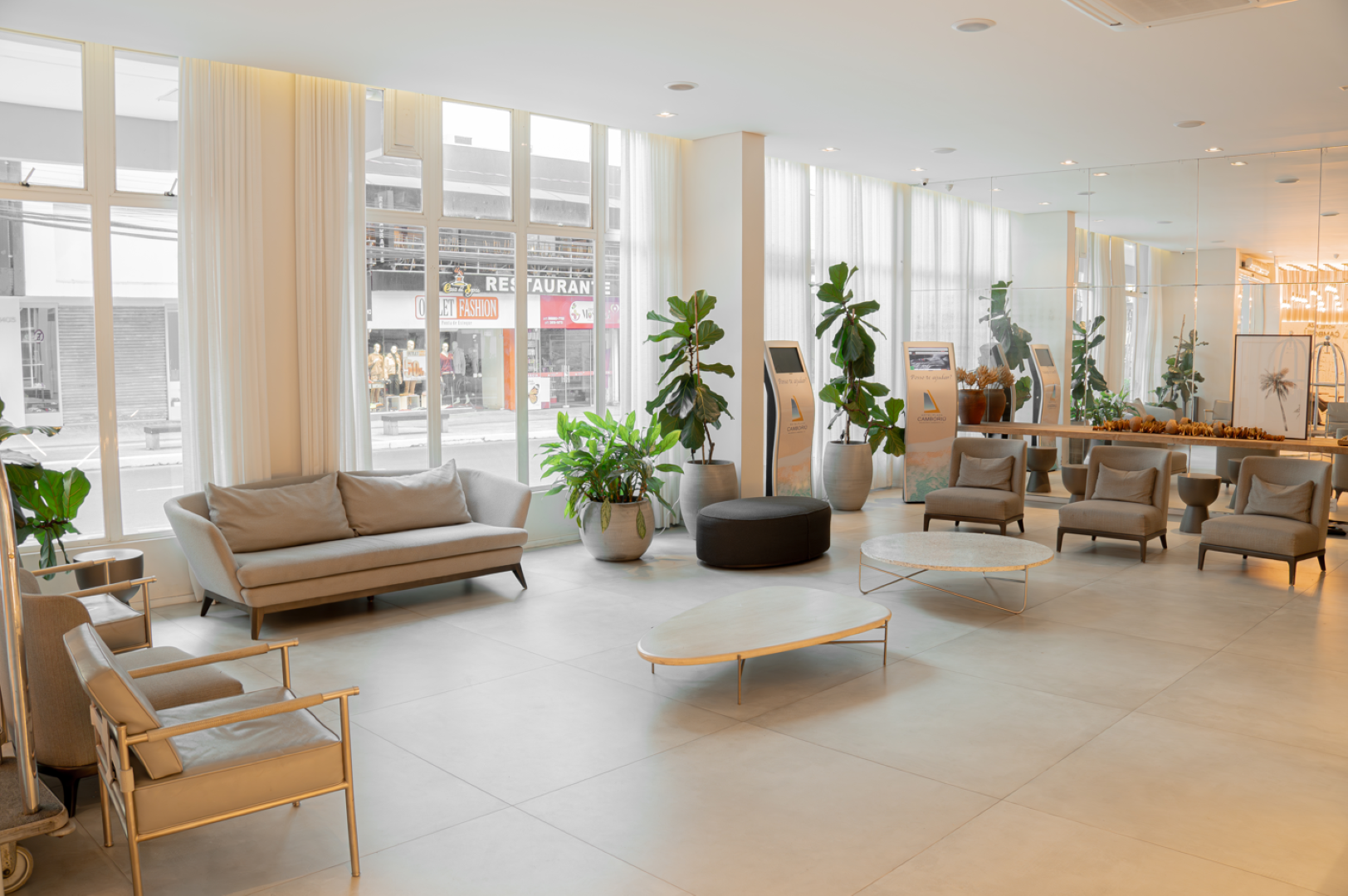 Sala de espera moderna e iluminada, com móveis de cores claras, janelas grandes e plantas em vasos.