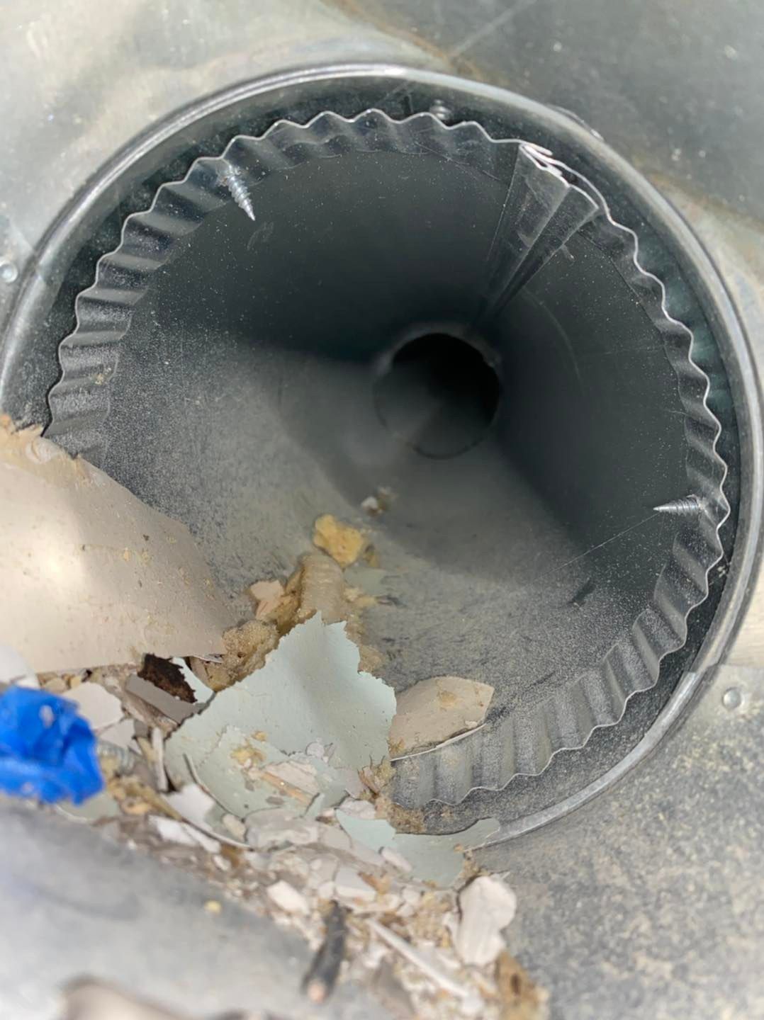 Close-up of a gray circular plastic vent or duct opening with debris around the rim.