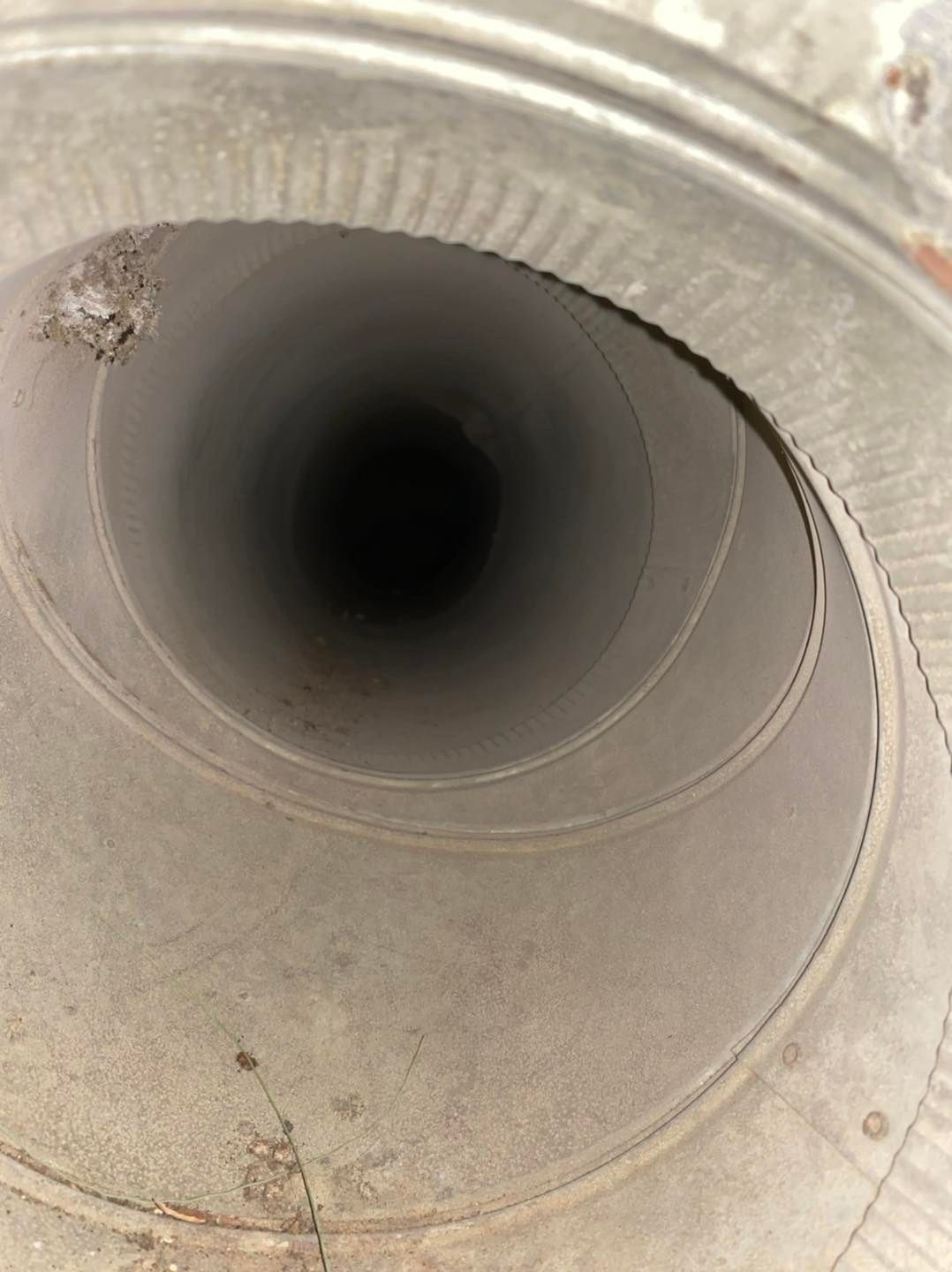Close-up of a metal duct opening with a dark circular interior and light gray, dusty edges