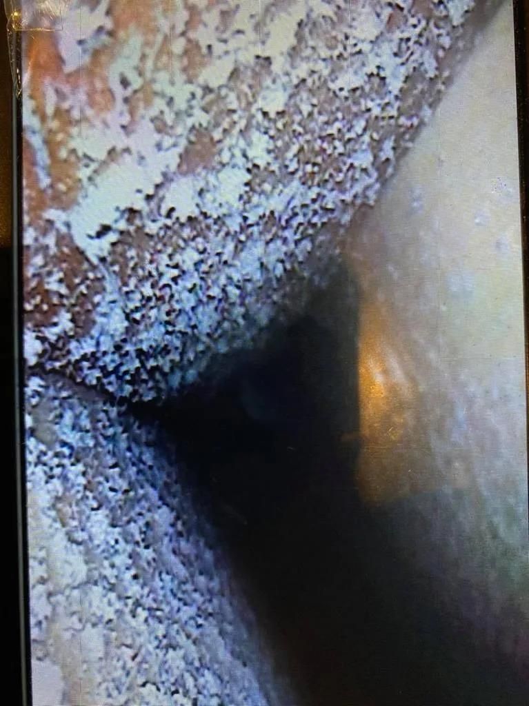 Close-up of a rusted, corroded metal opening with a dark center and frosty residue on the edges