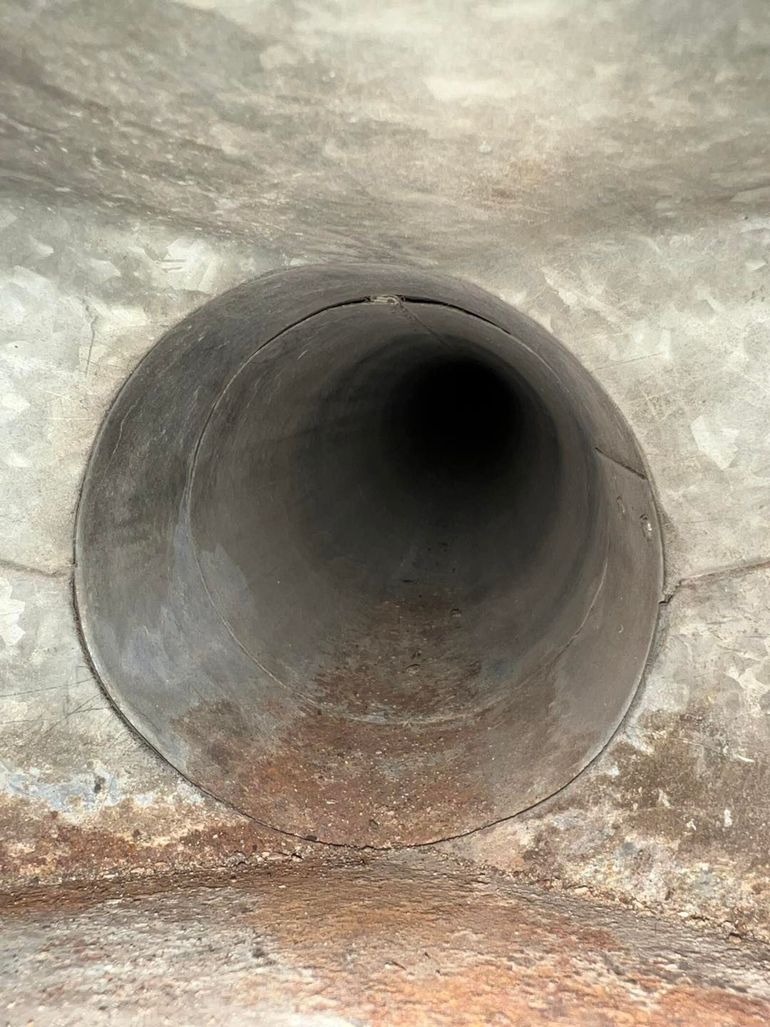 Circular metal pipe opening with rust at the bottom, viewed from the inside.