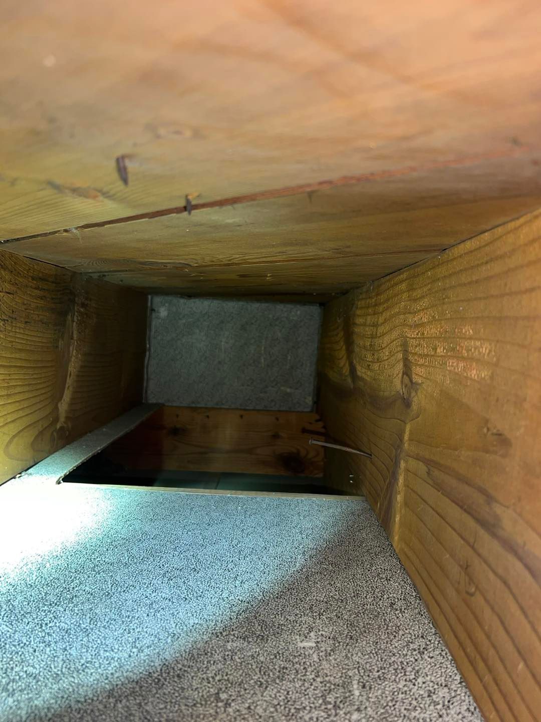Inside a wooden vent or duct with a gravel floor and a square opening at the far end.