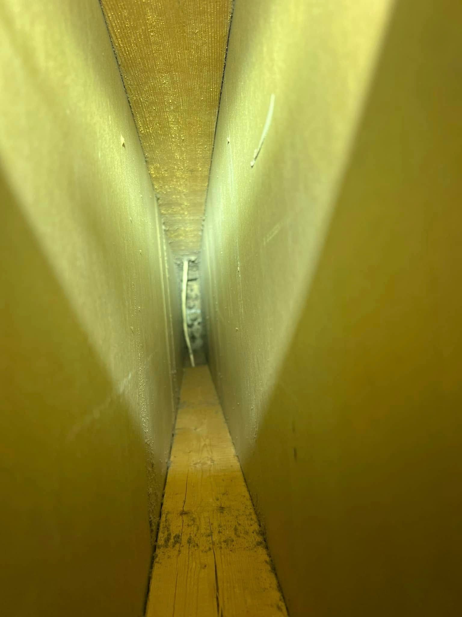 Narrow yellow corridor with slanted walls and a small vent or opening at the far end