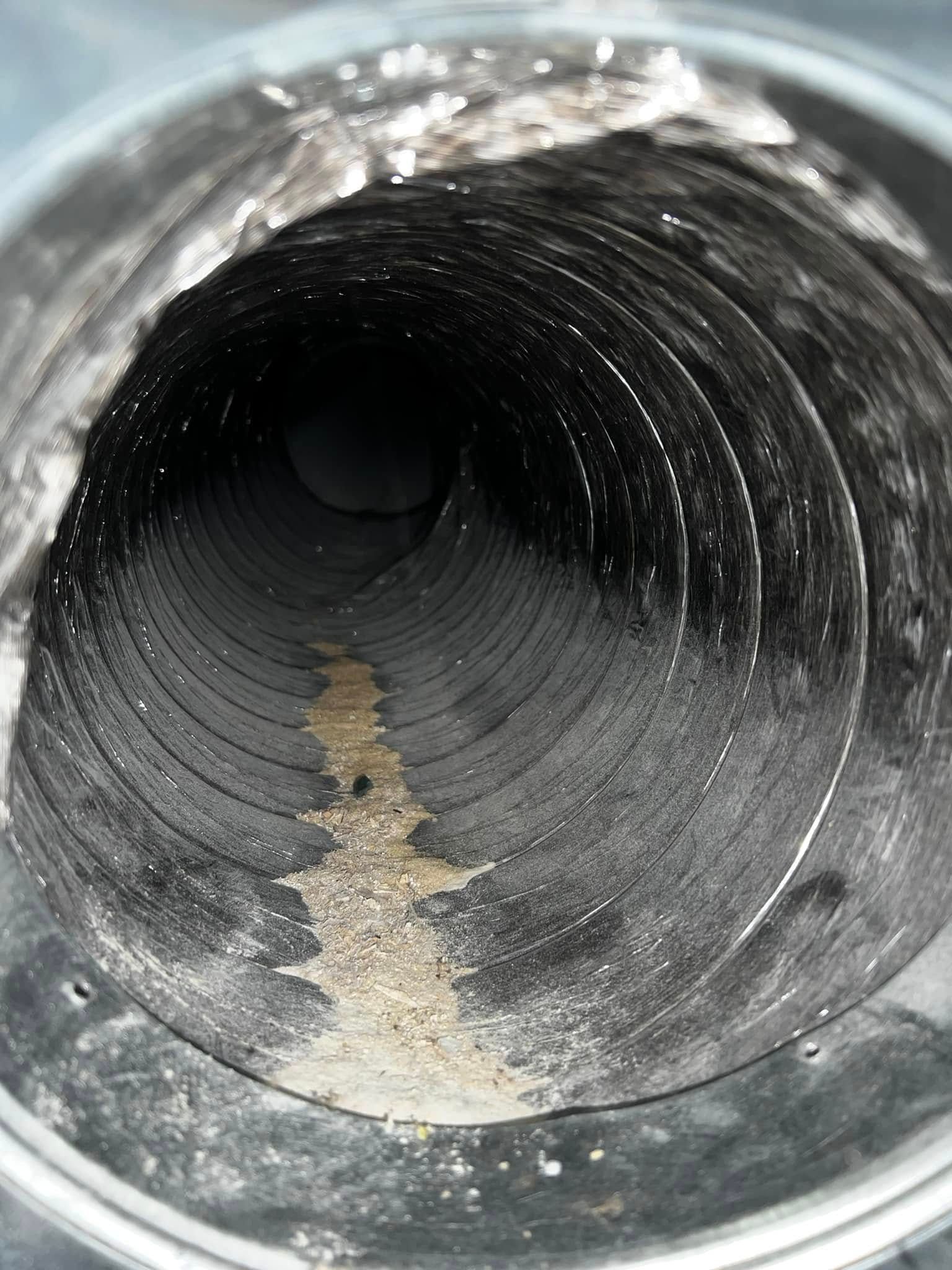 Inside of a black corrugated pipe with dust and a tan debris strip running through the center